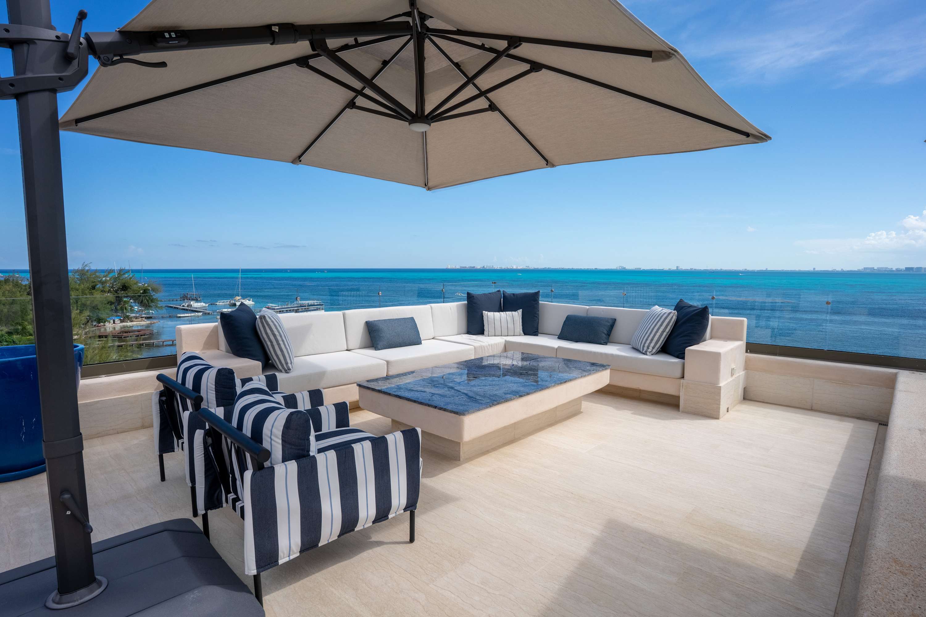 An outdoor patio with white sectional sofa, striped chairs, and a blue marble coffee table overlooki