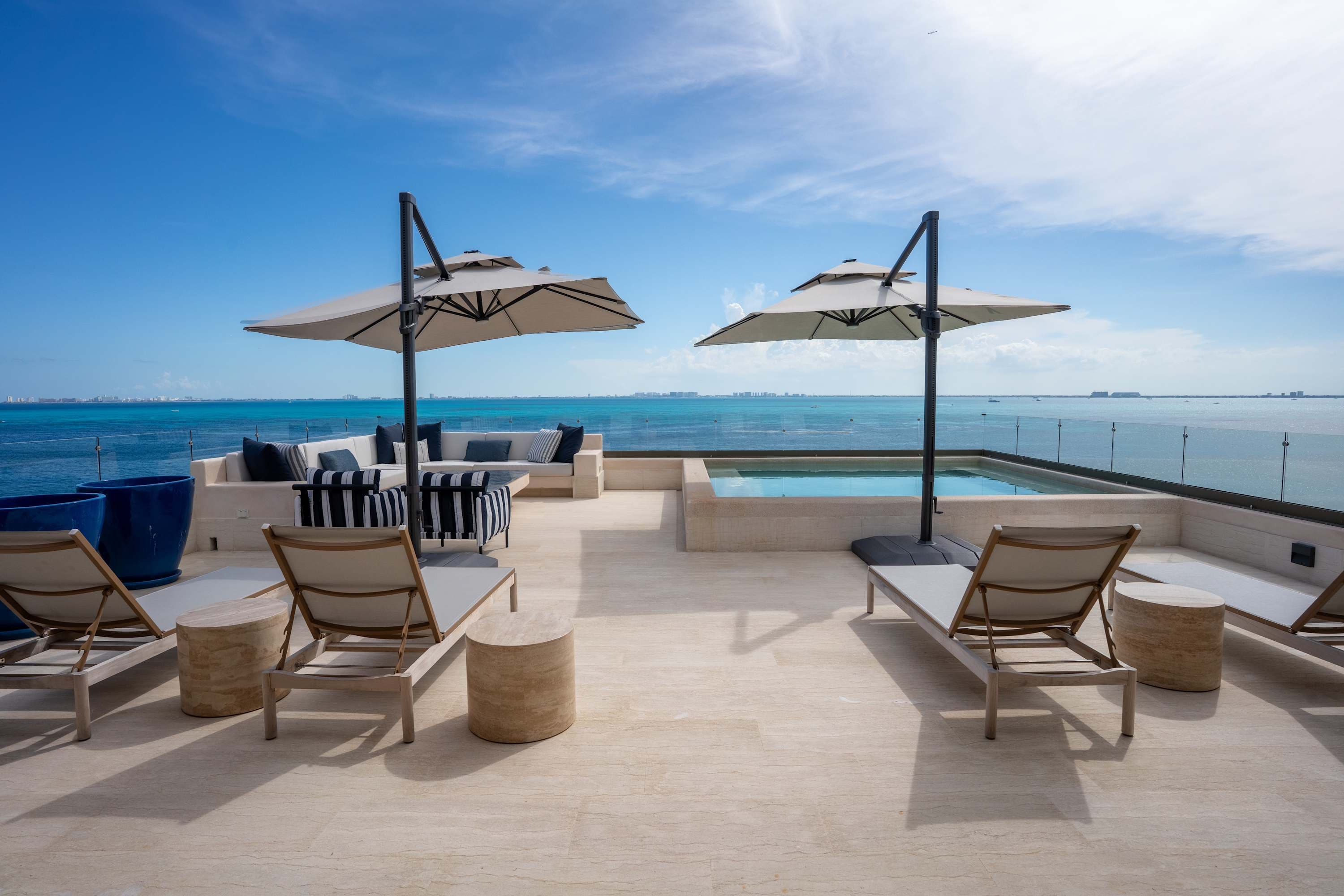 Rooftop terrace with lounge chairs, umbrellas, a pool, and a view of the ocean.