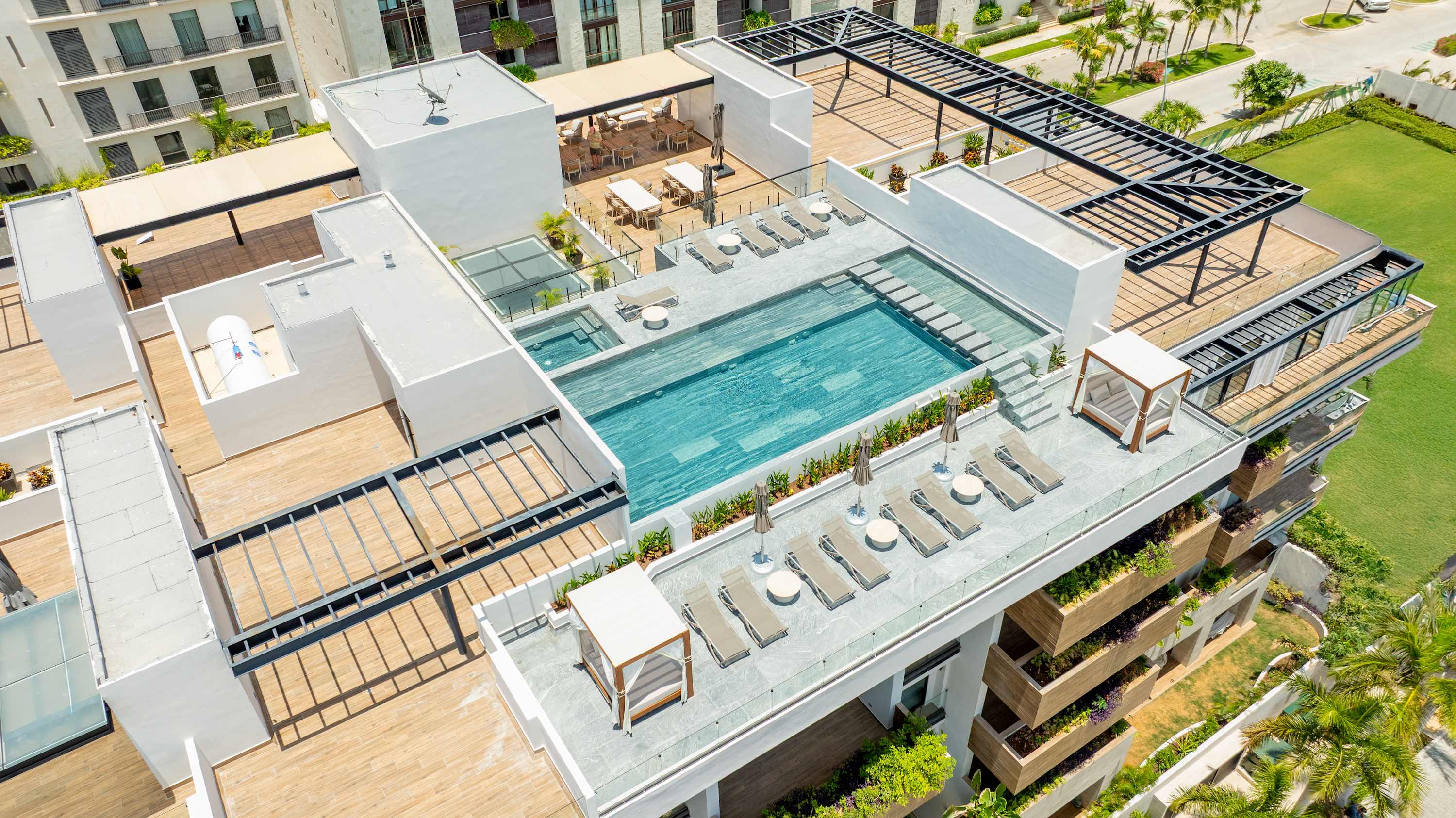 Rooftop pool with lounge chairs and cabana, surrounded by buildings and lush greenery.