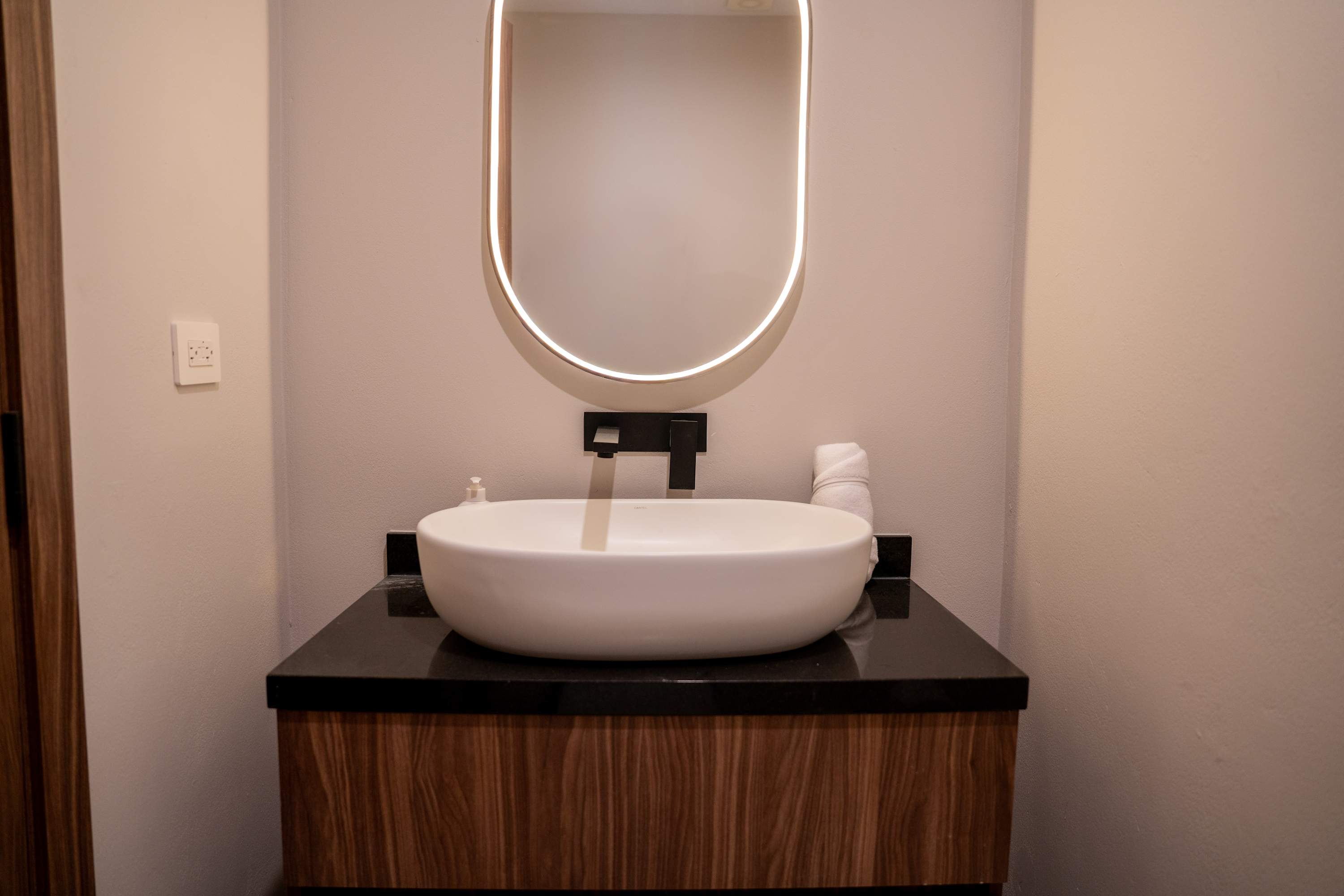 A modern bathroom vanity with a white vessel sink, black faucet, and wooden cabinet.