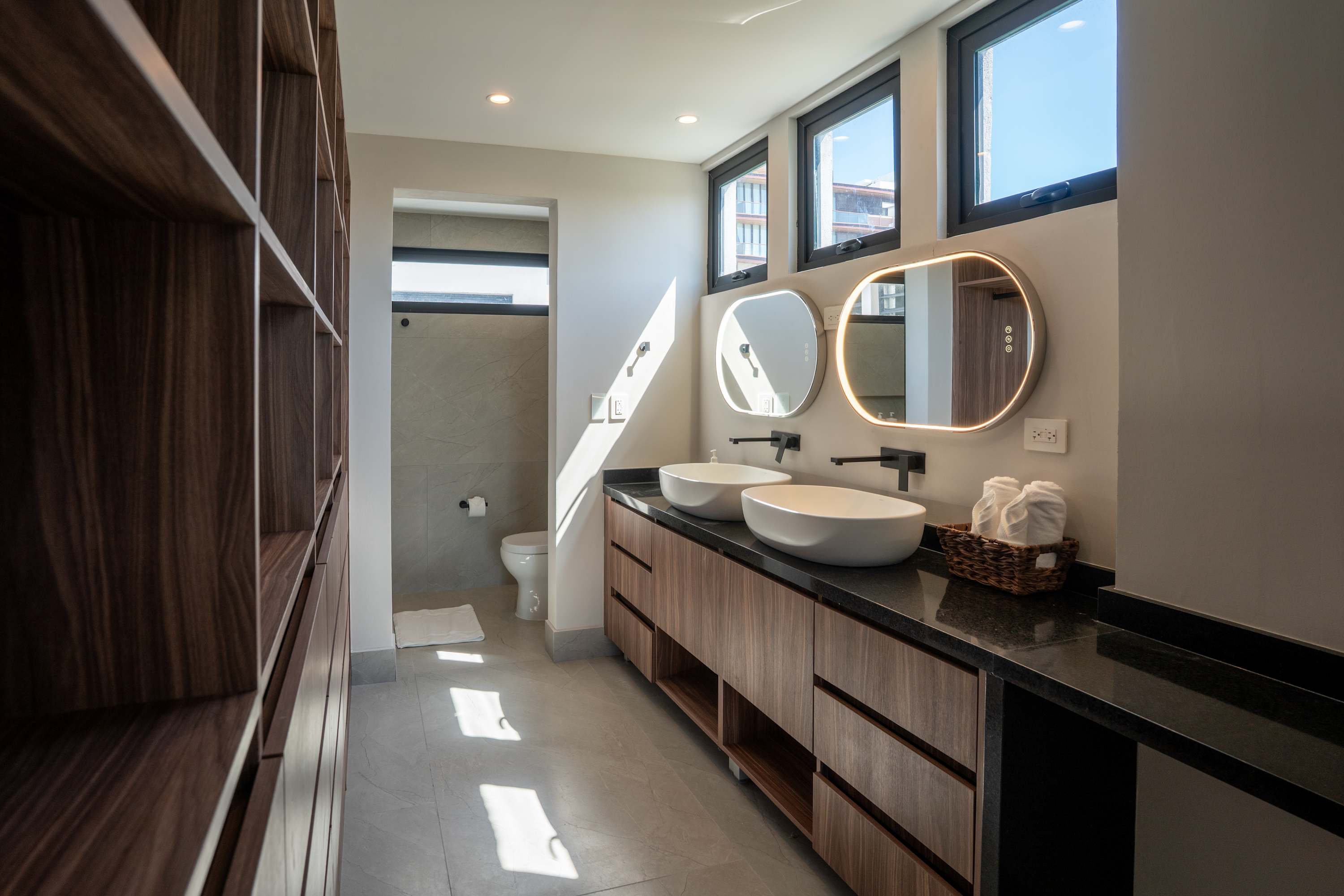 Modern bathroom with double vanity, mirrored cabinets, and a private toilet room.