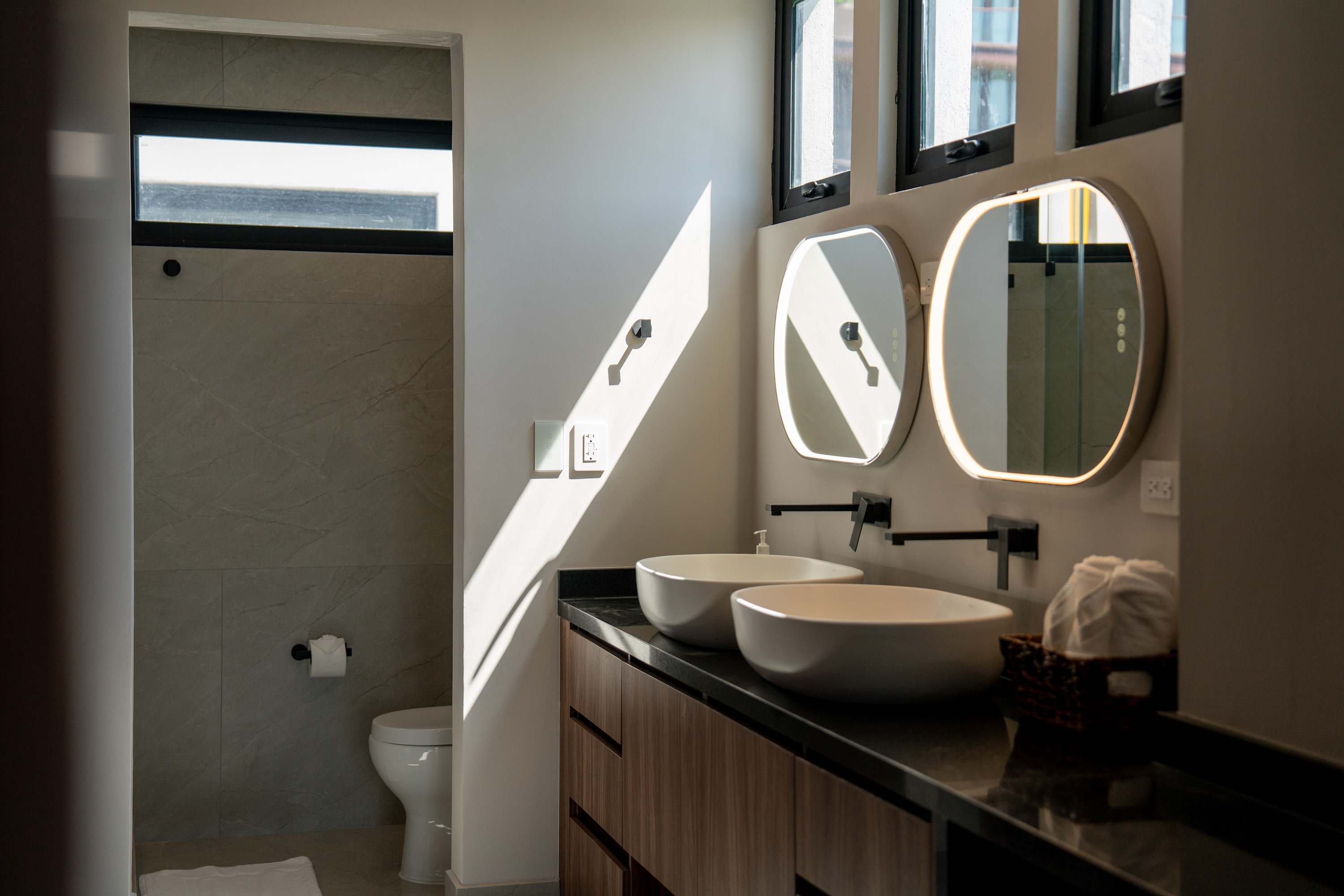 Modern bathroom with dual sinks, wall-mounted faucets, and backlit mirrors.
