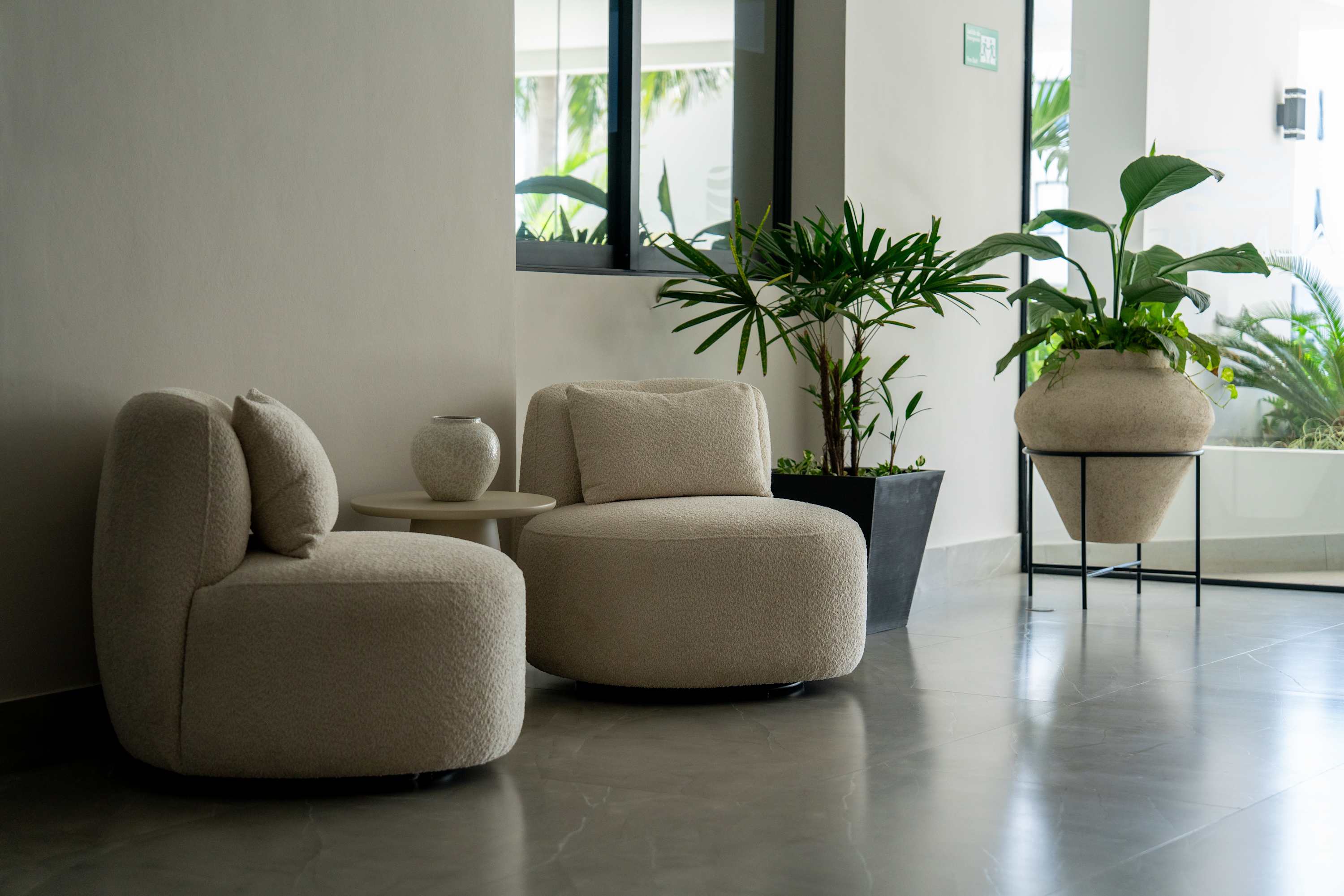 Two cream boucle chairs sit in a modern lobby with large potted plants.