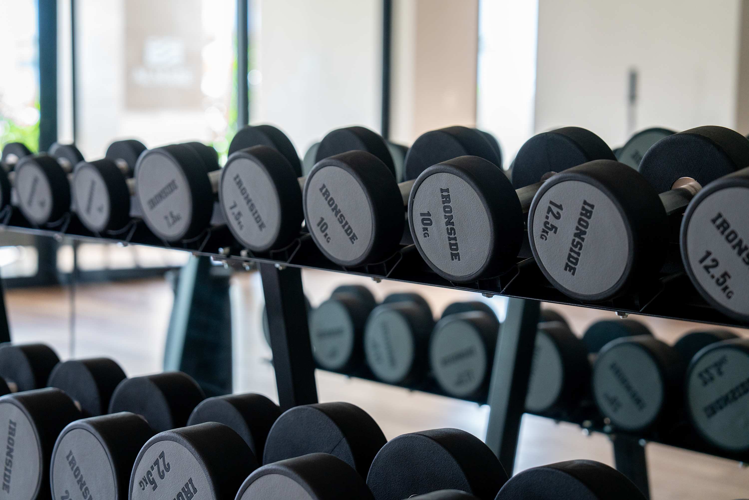 Dumbbell rack with various weights, some labeled "IRONSIDE" and weights like 7.5kg, 10kg, 12.5kg, an