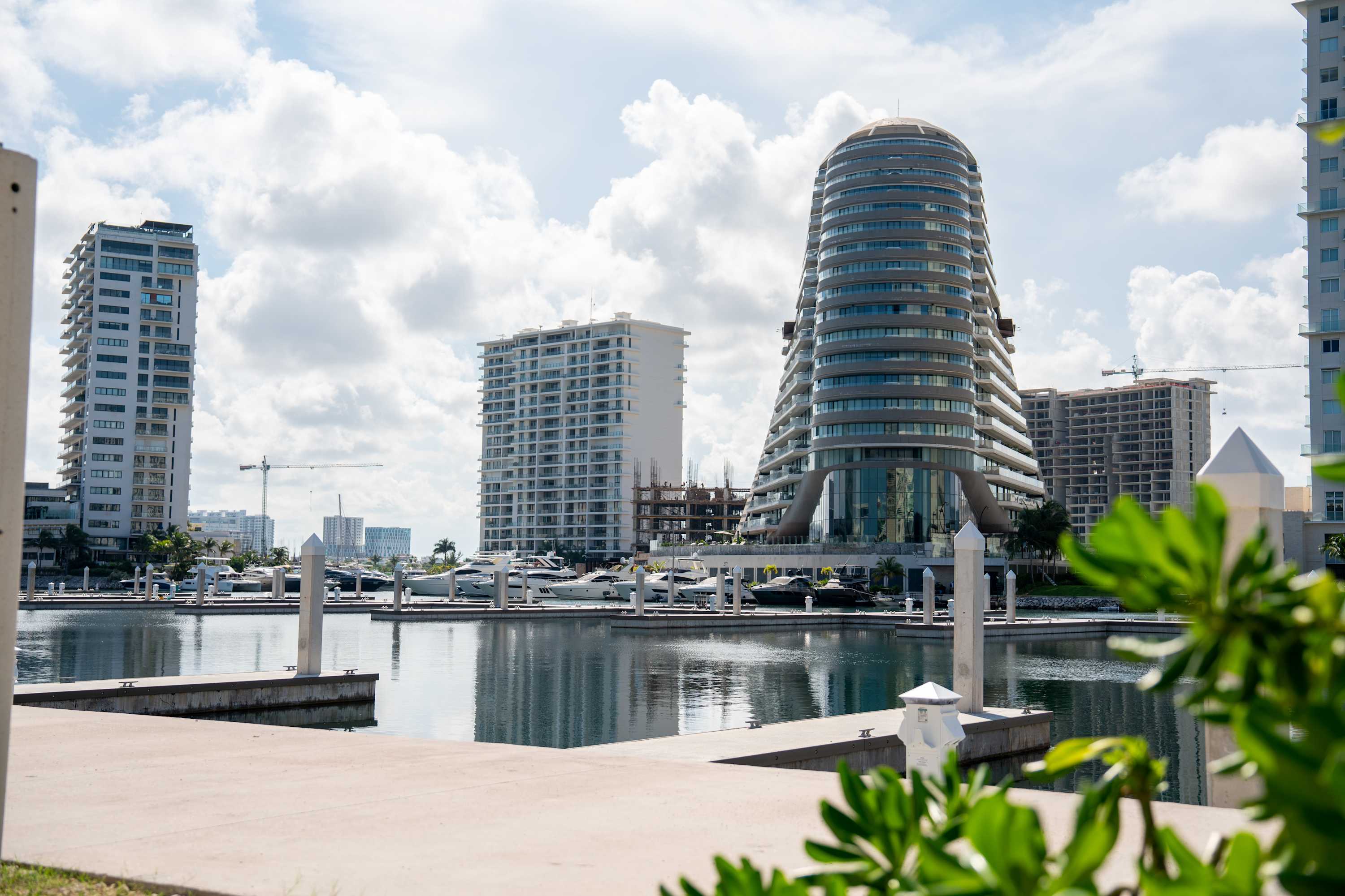 Boats docked at a marina with modern buildings in the background.
