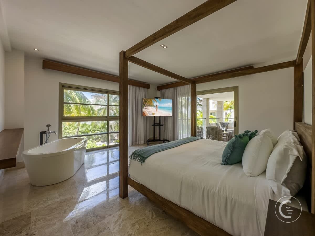 Bedroom with a bathtub, a large bed, and a view of palm trees.