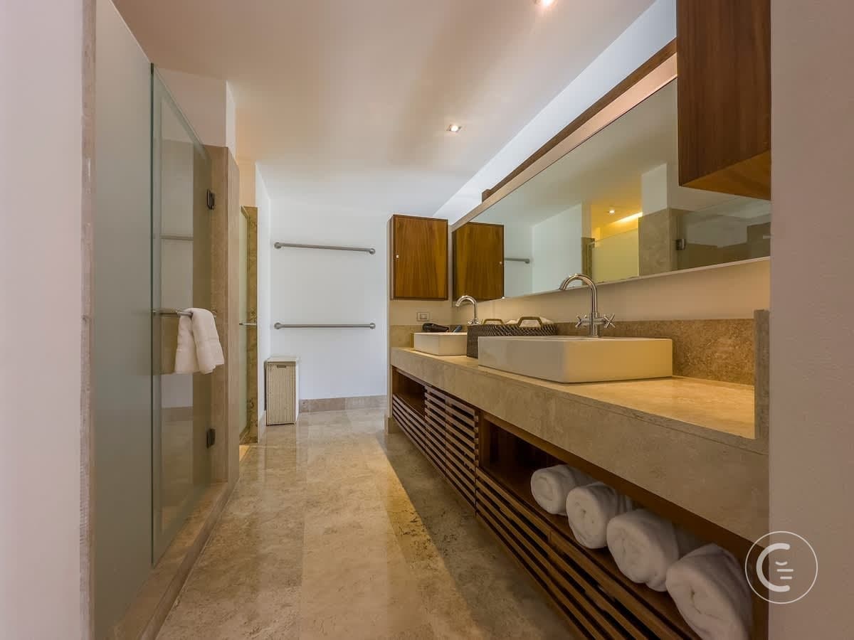 A modern bathroom with a glass shower, double sinks, and wooden cabinetry.