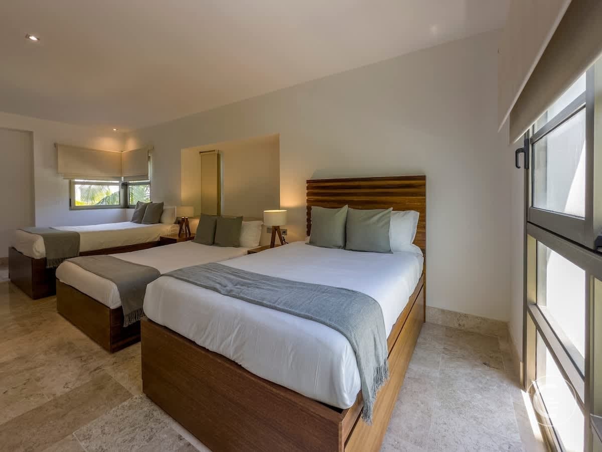 A bedroom with three beds, each with white linens and a grey throw blanket.