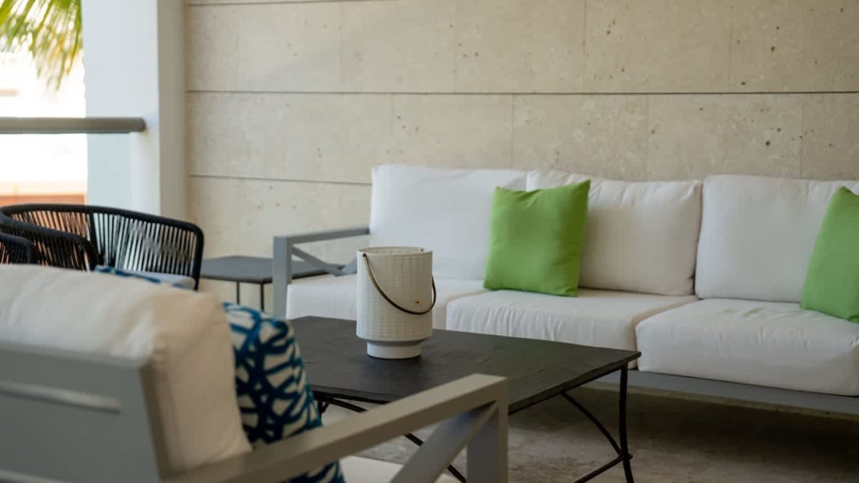 Outdoor patio furniture, including a white couch and dark chairs, with green pillows and a coffee ta