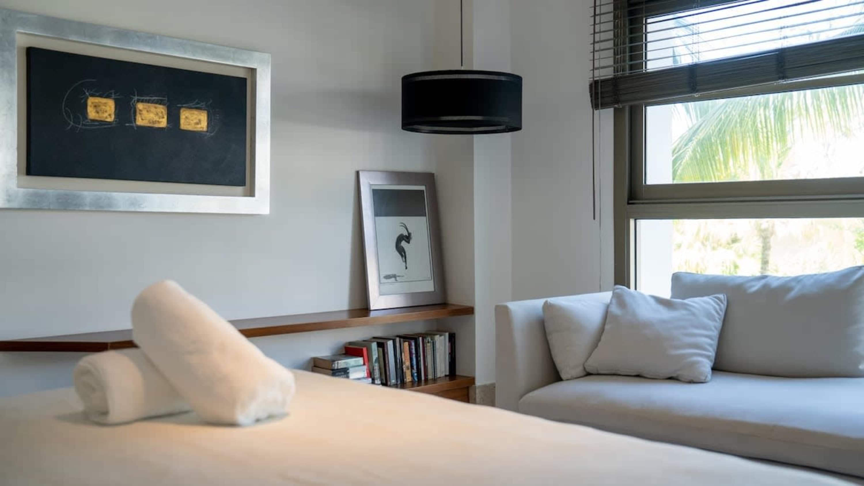 Modern room with artwork, books, and a couch overlooking palm trees.