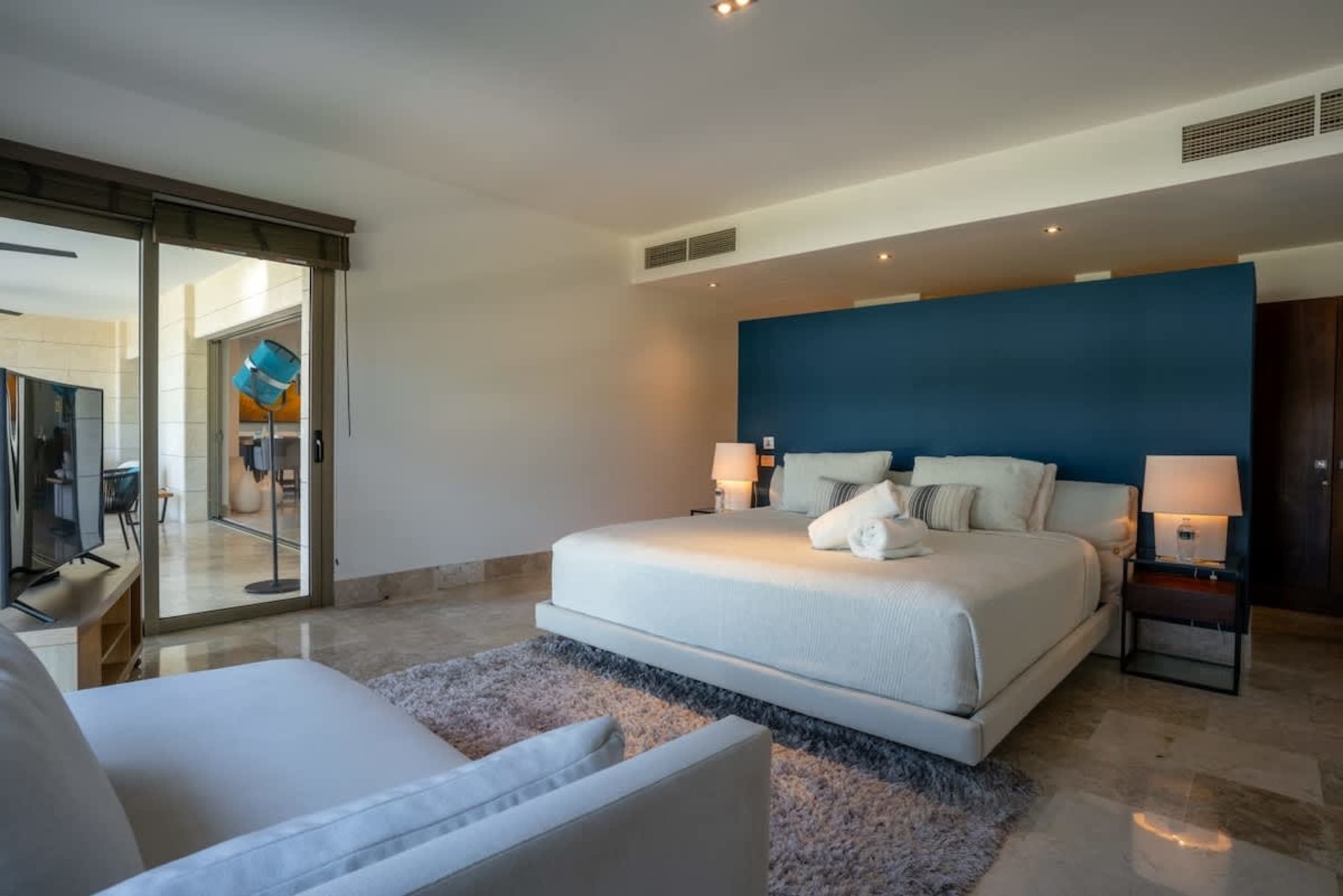 Modern bedroom with a king-size bed, blue accent wall, and a large sliding glass door.