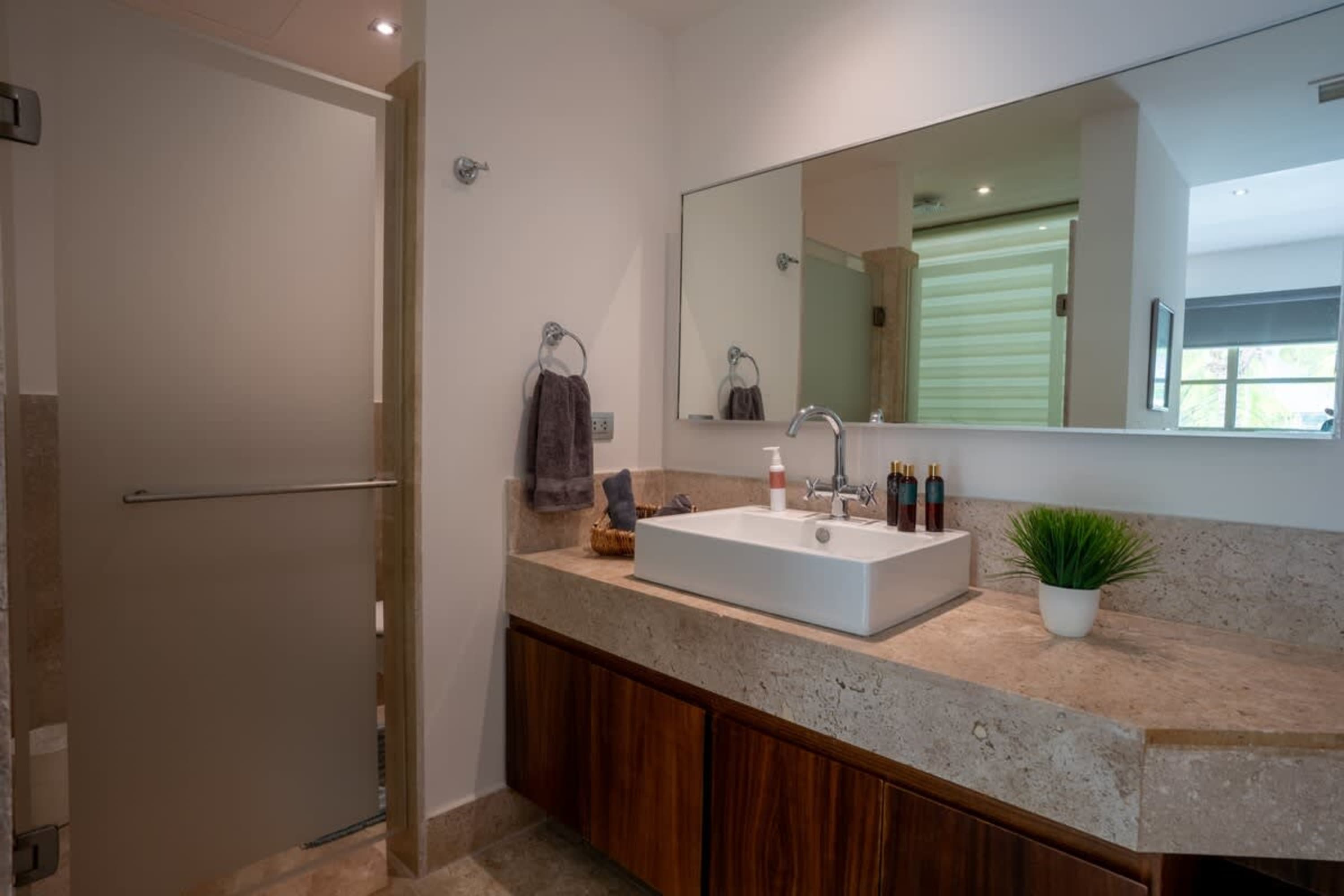 A modern bathroom with a white square sink, wooden cabinets, and a large mirror.