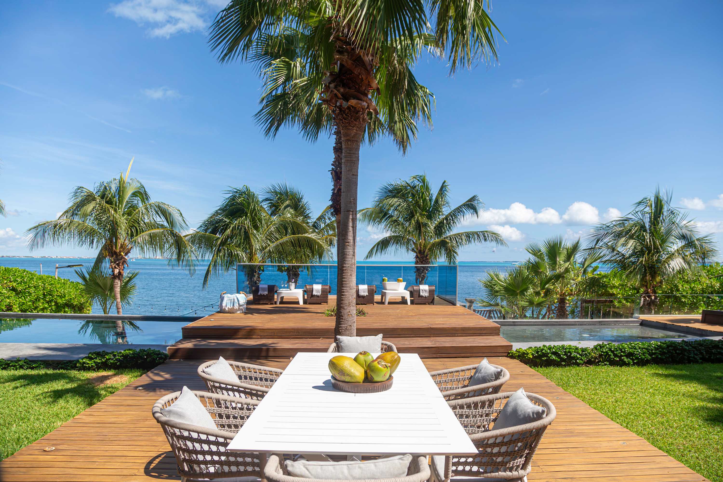 Outdoor dining area with table, chairs, and palm trees by the ocean.