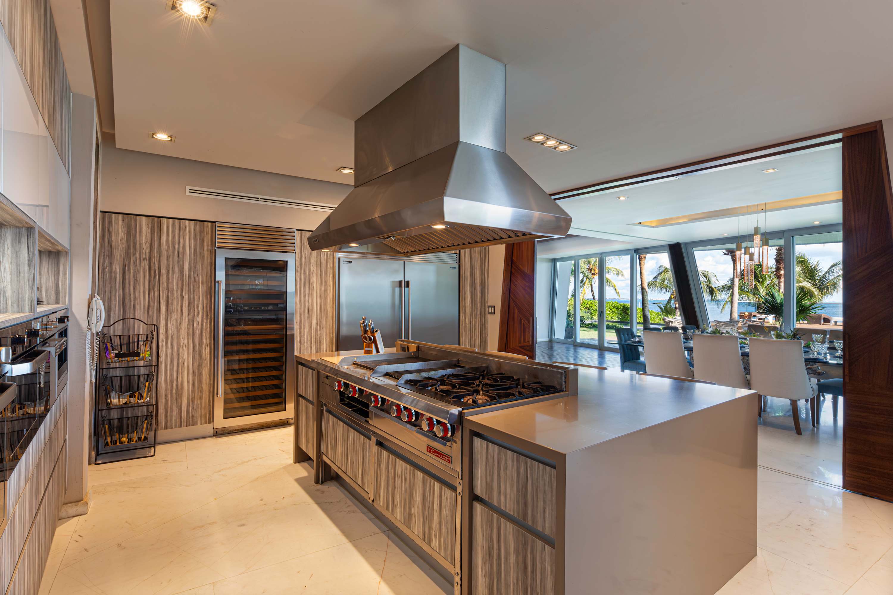 A modern kitchen with a large island and stainless steel appliances, leading to a dining area with o