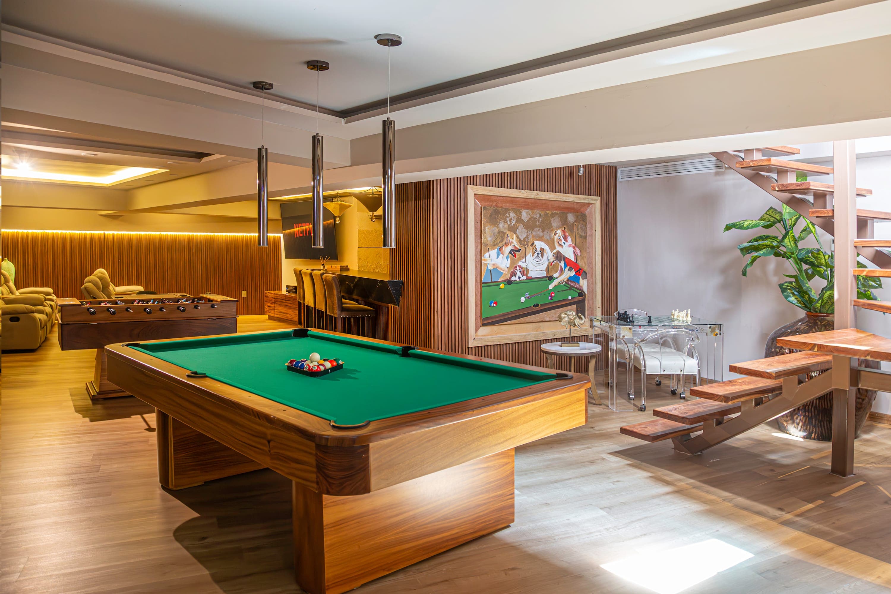 A spacious recreation room with a pool table, foosball table, and a modern staircase.