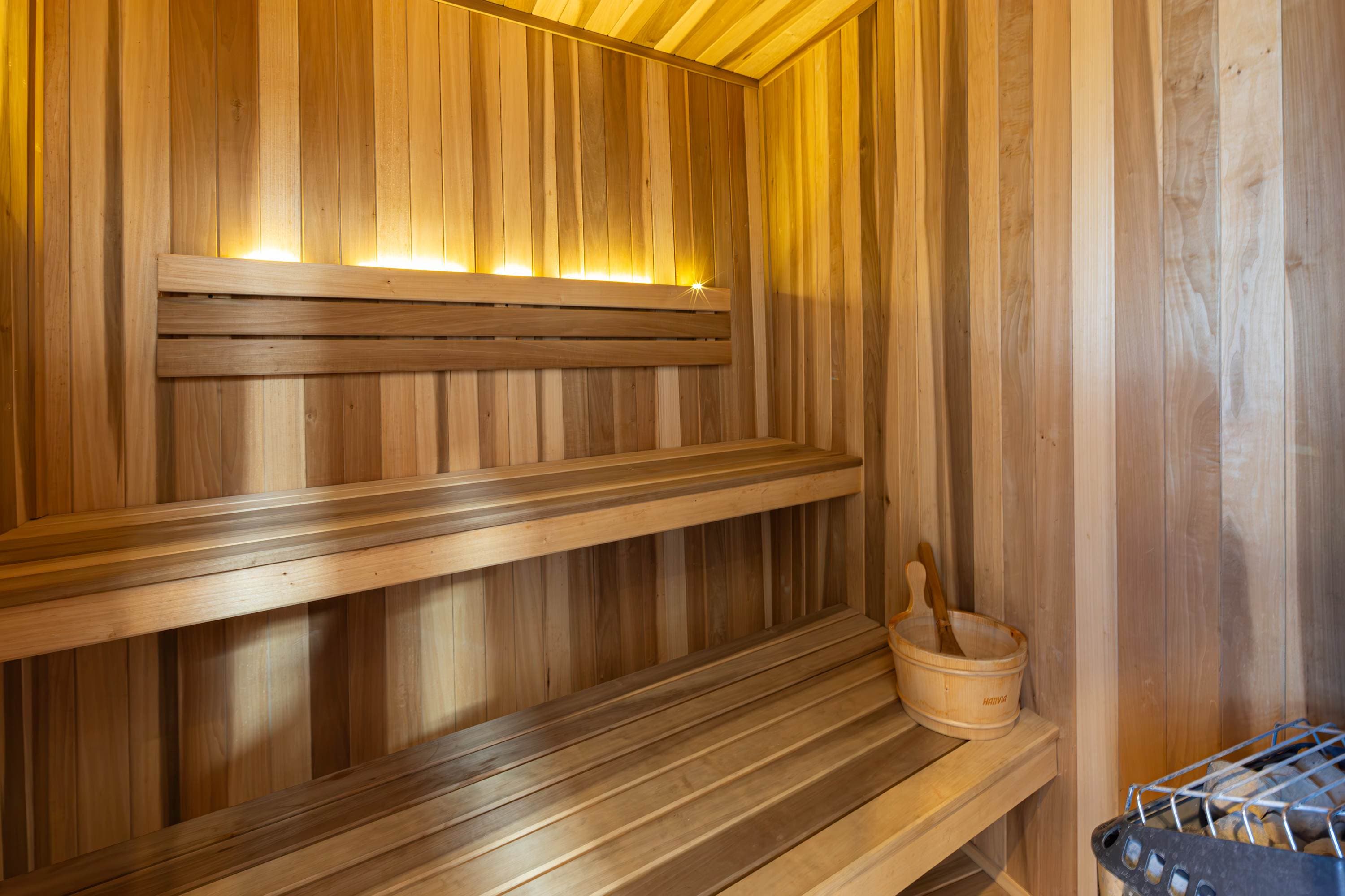 Interior of a wooden sauna with two tiers of benches, a bucket, and a heater.
