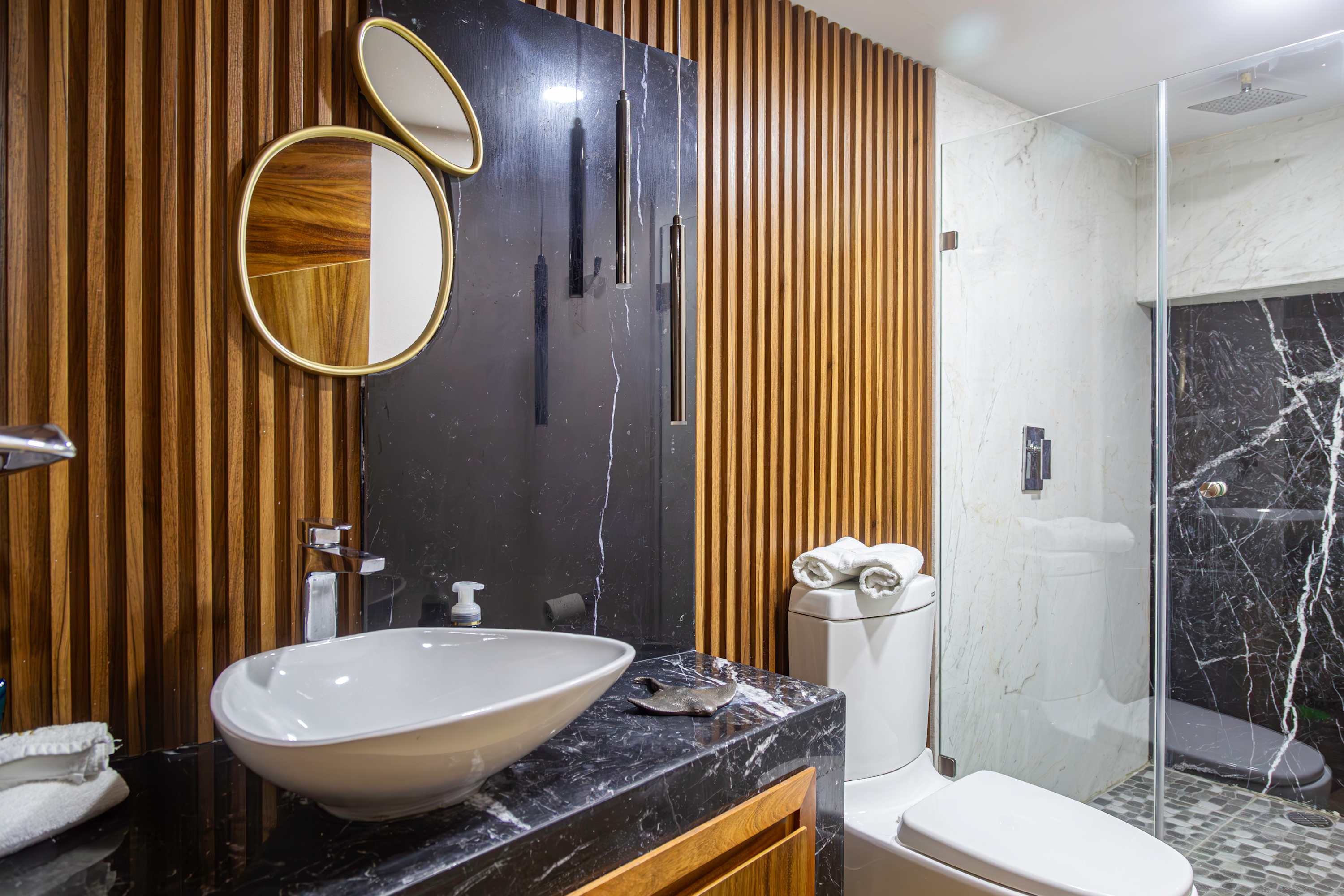 Modern bathroom with wood accent wall, marble vanity, and glass shower enclosure.