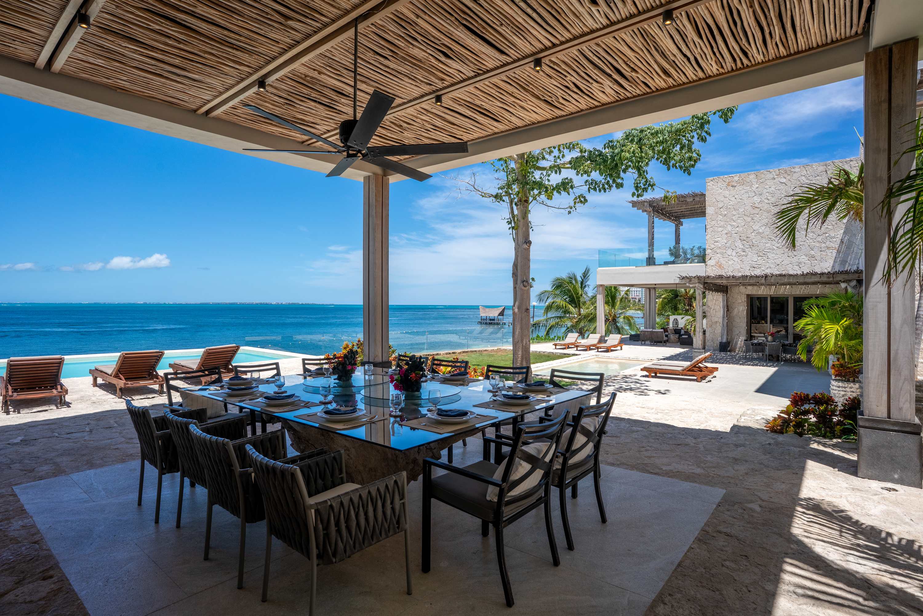 Dining table and chairs under a thatched roof with ocean views.