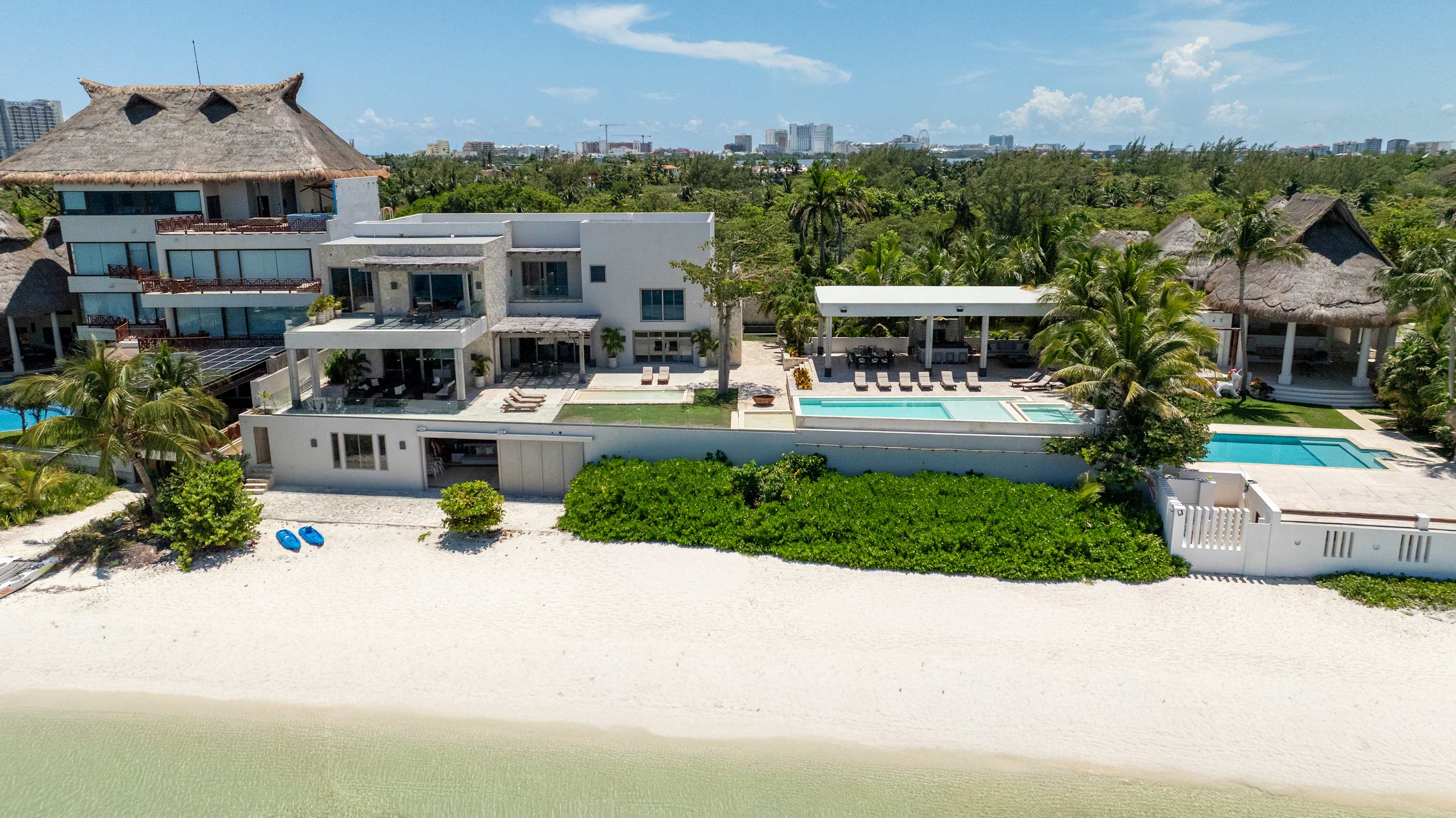 Luxury beachfront villa with multiple pools, thatched-roof architecture, and ocean views.