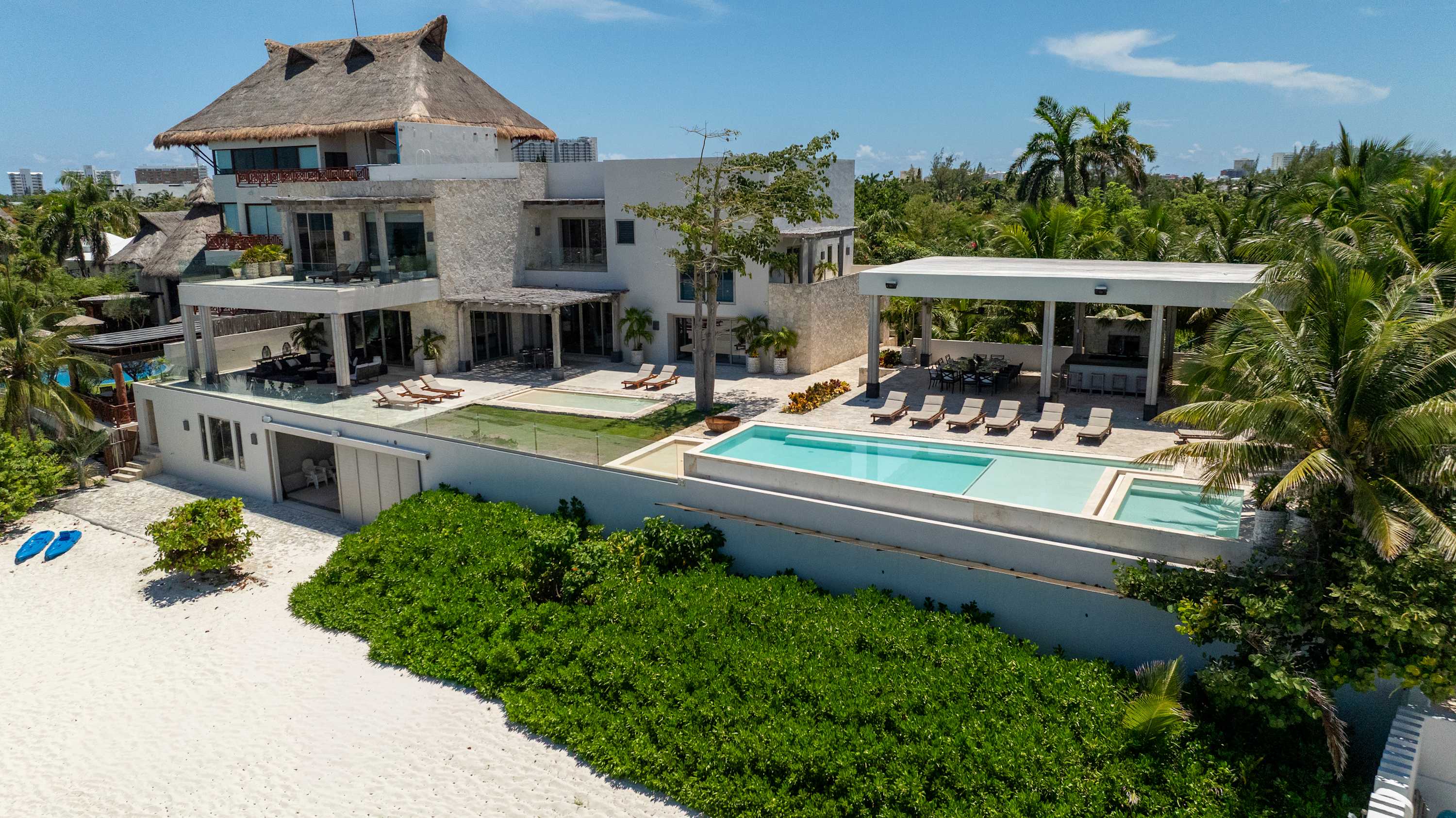 Modern luxury villa with thatched roofs, multiple pools, and beach access.