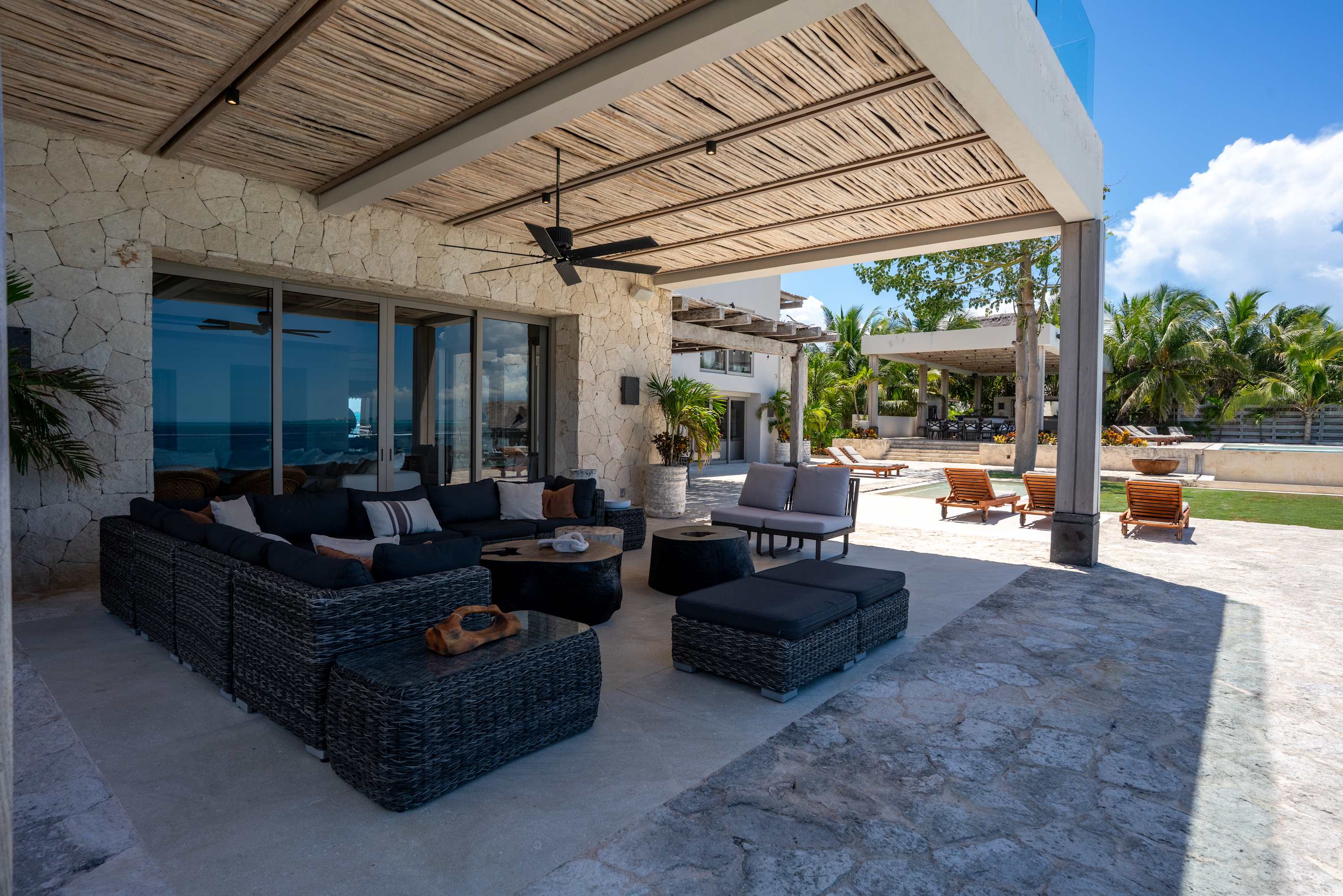 Outdoor patio with wicker furniture, stone walls, and a thatched roof.