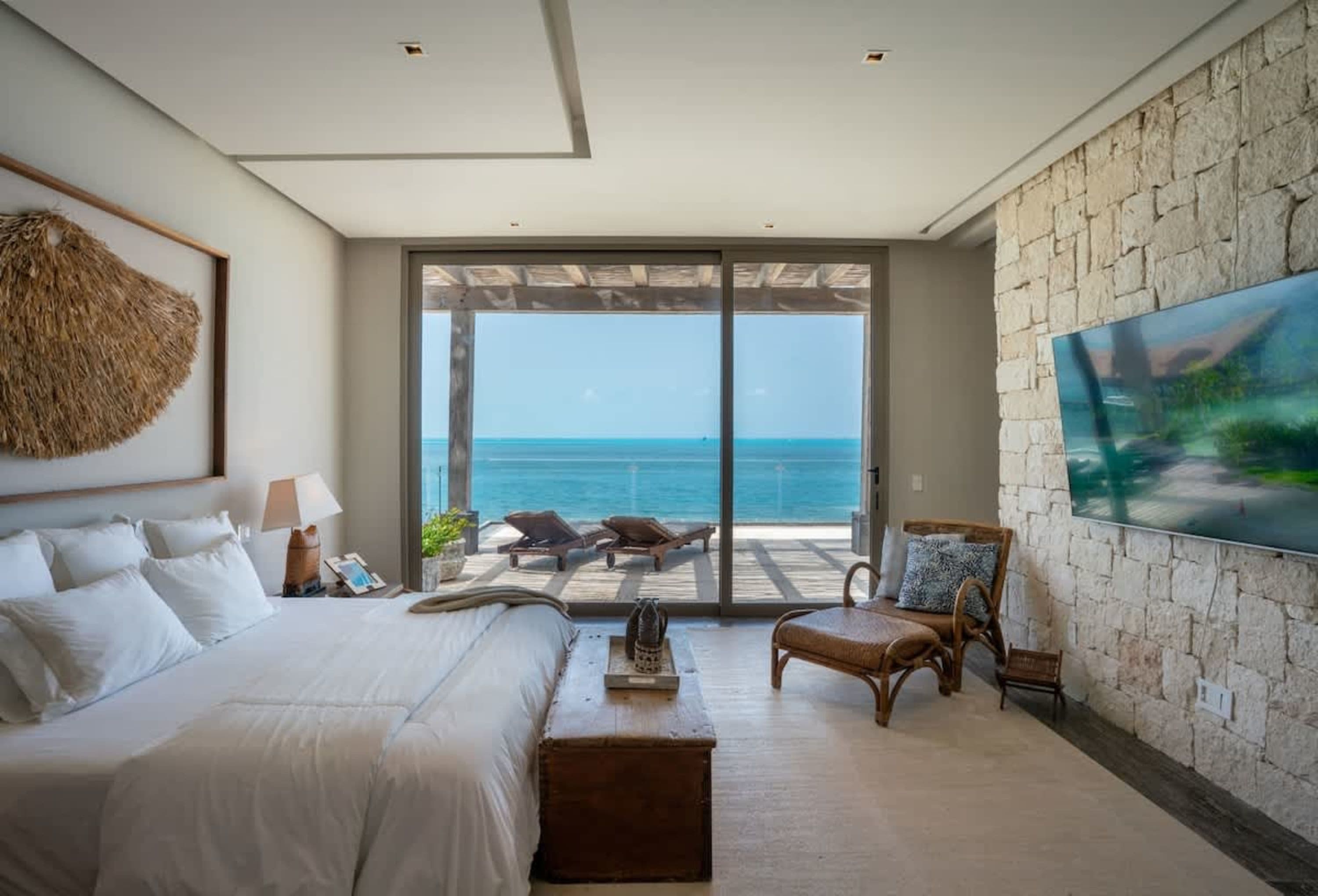 A serene bedroom with a large sliding glass door opening to the ocean.