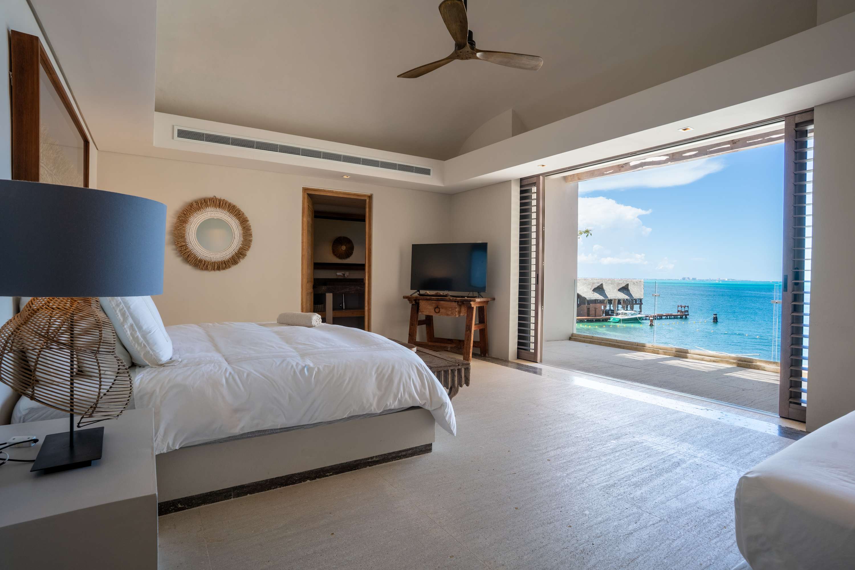 Modern bedroom with a king-size bed and a large glass door leading to a tropical ocean view.
