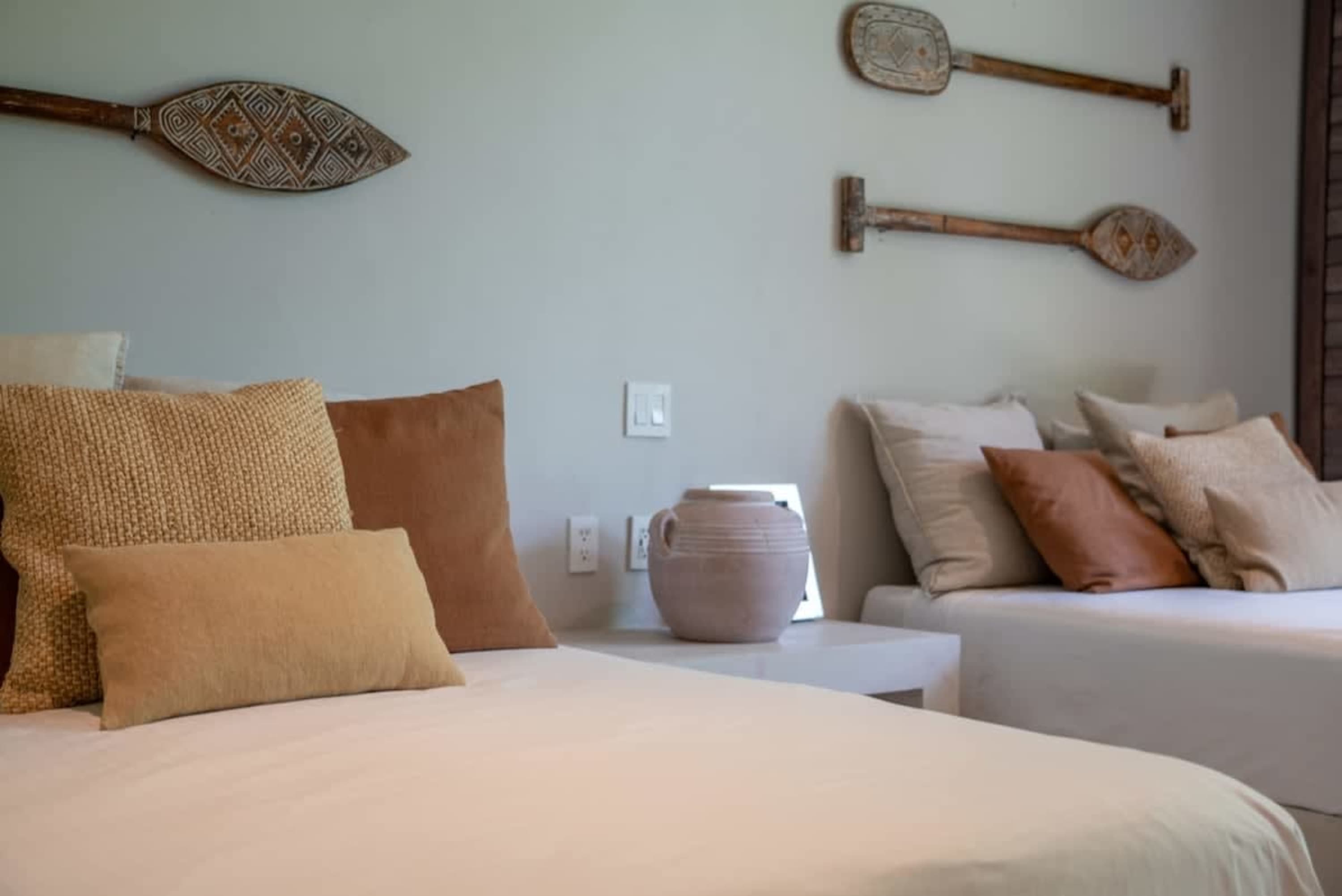 Two beds with neutral-toned pillows and decorative paddles on the wall.