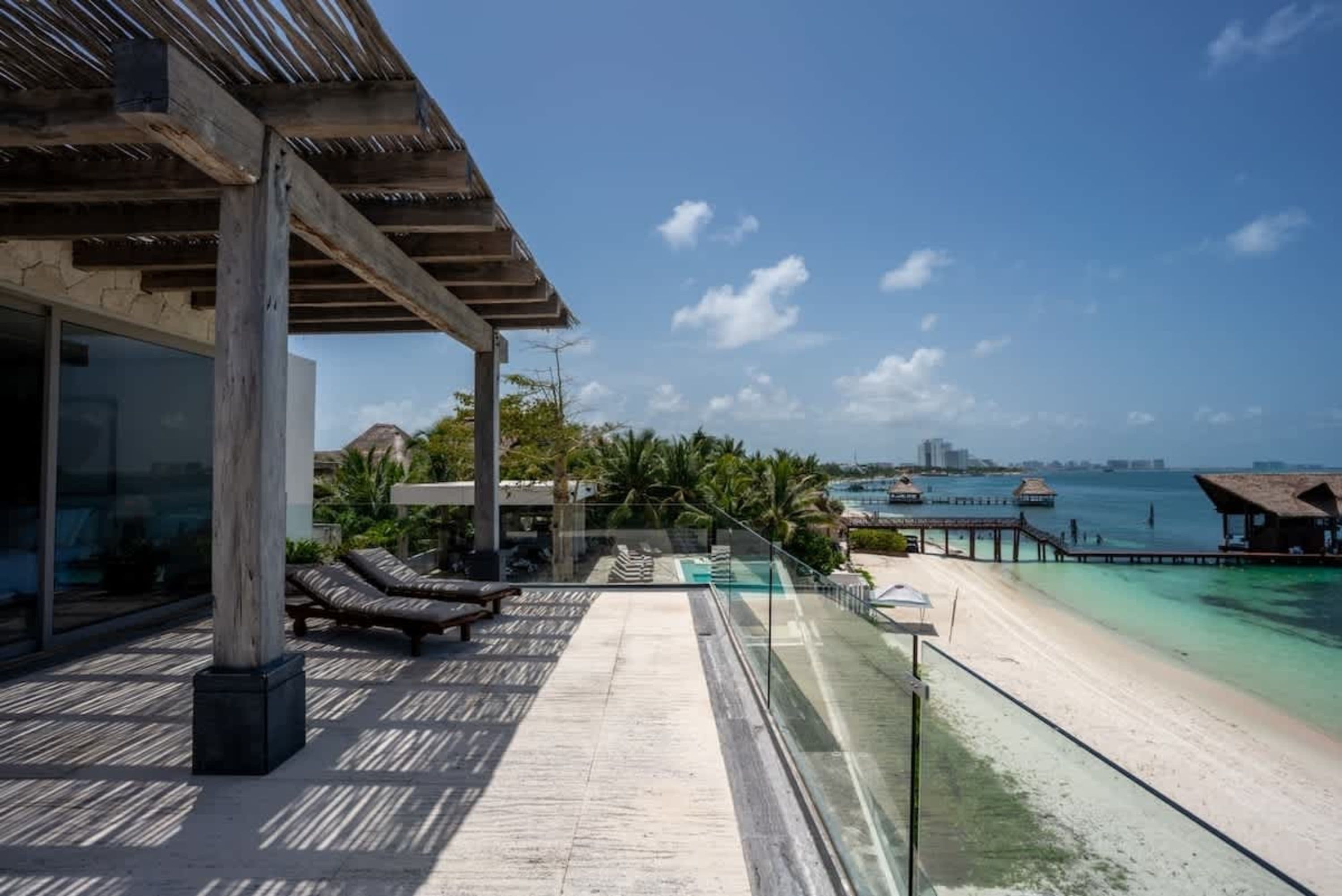 Oceanfront property with a wooden pergola, lounge chairs, and a clear blue sky.