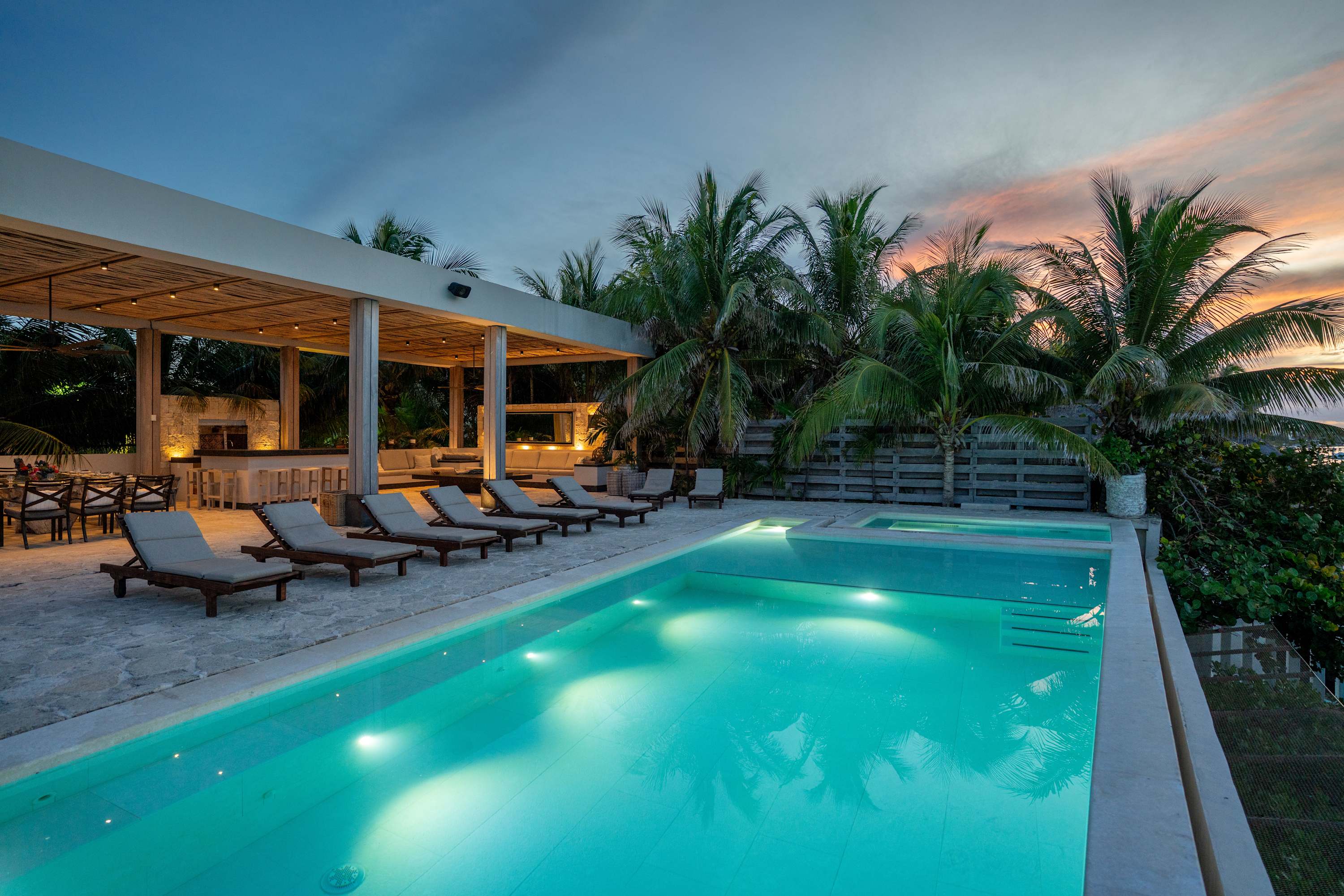 A beautiful infinity pool at dusk with palm trees and a bar area.