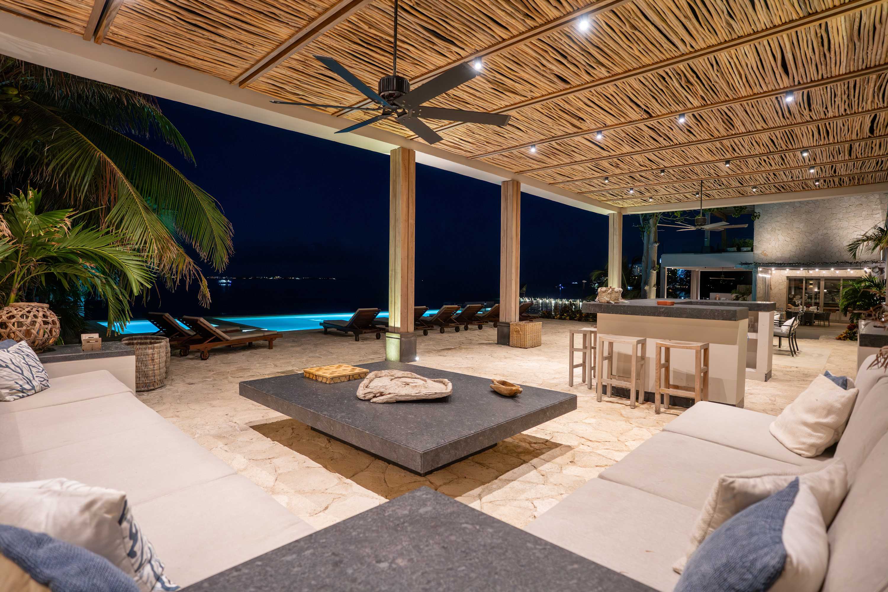 A covered patio with a pool and ocean view at night.