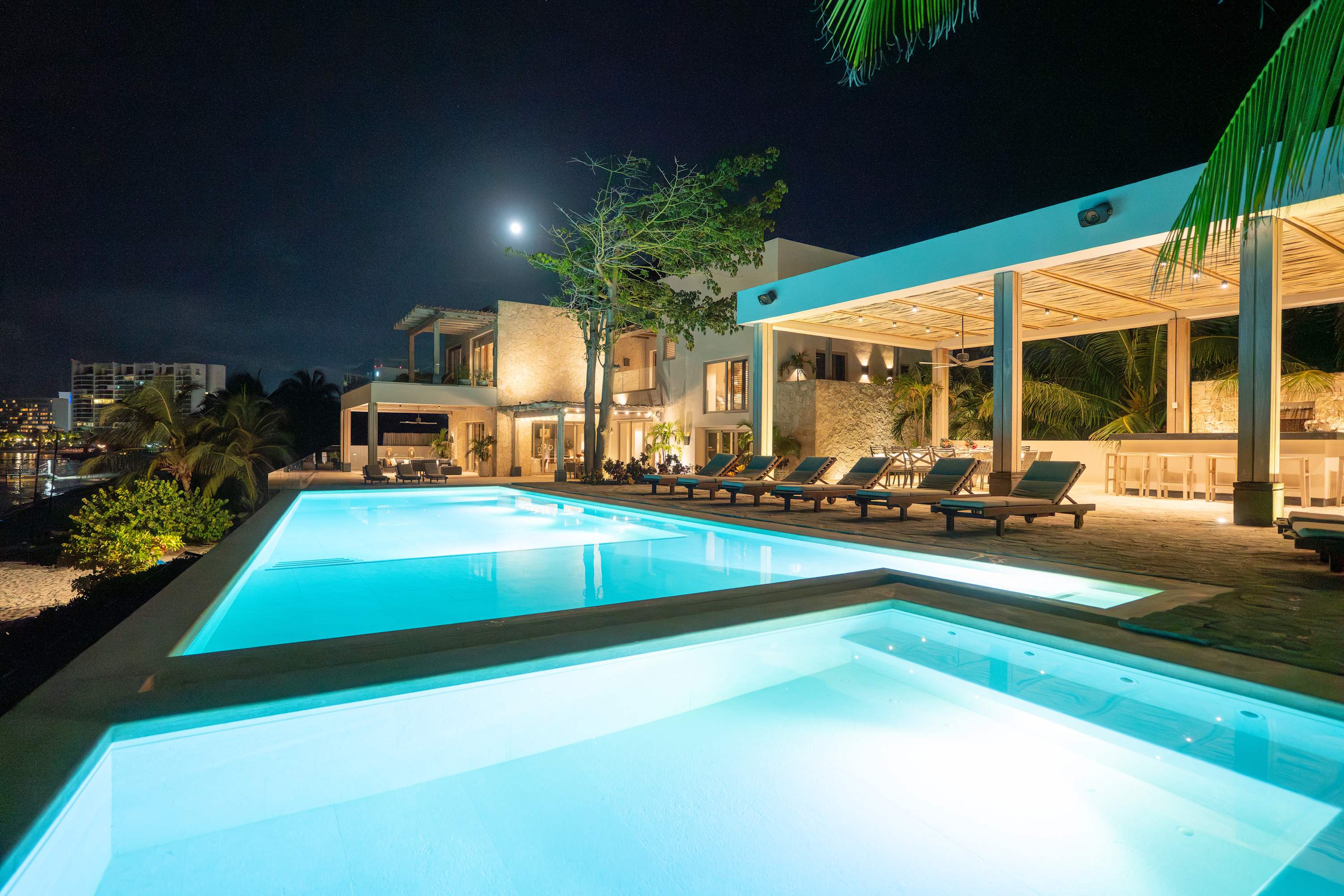A luxurious infinity pool reflects the moonlit sky at night at a modern villa.