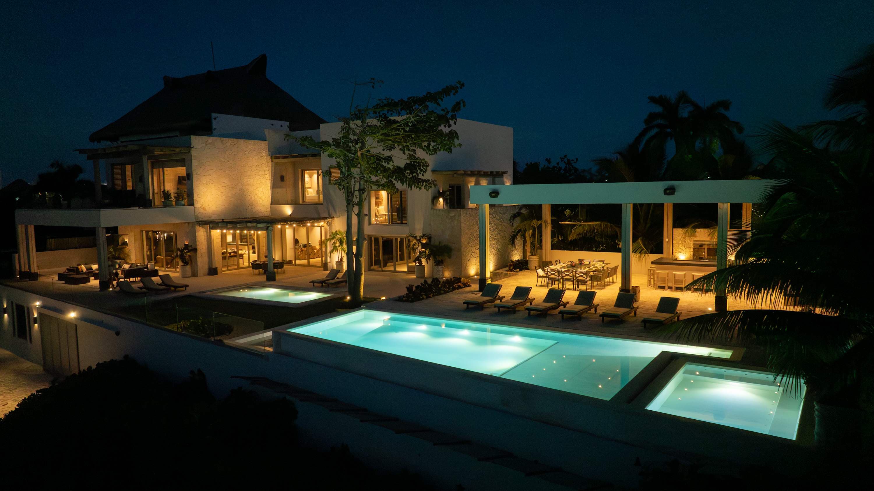 Luxury villa with pools and outdoor dining at night.