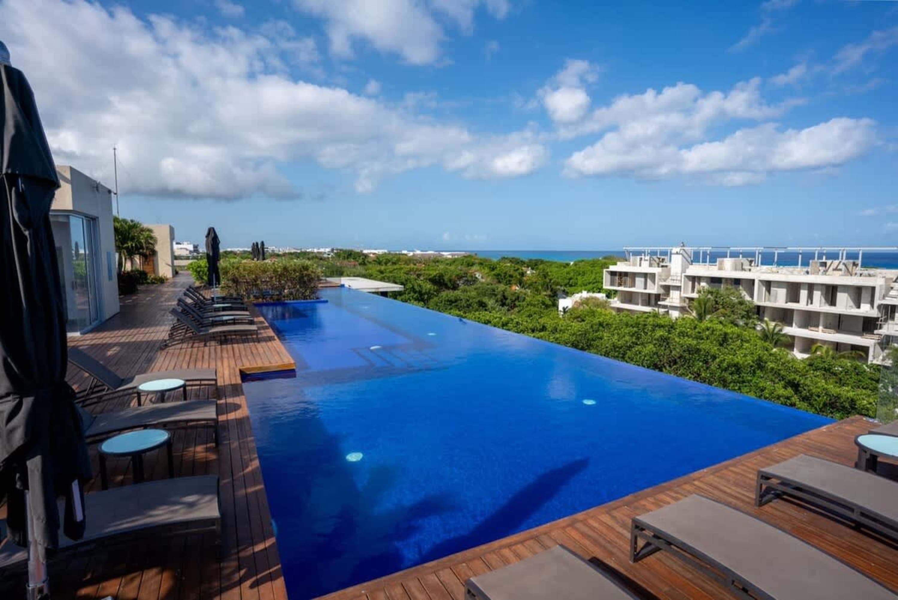 Infinity pool overlooking lush greenery and ocean, with lounge chairs on a wooden deck.