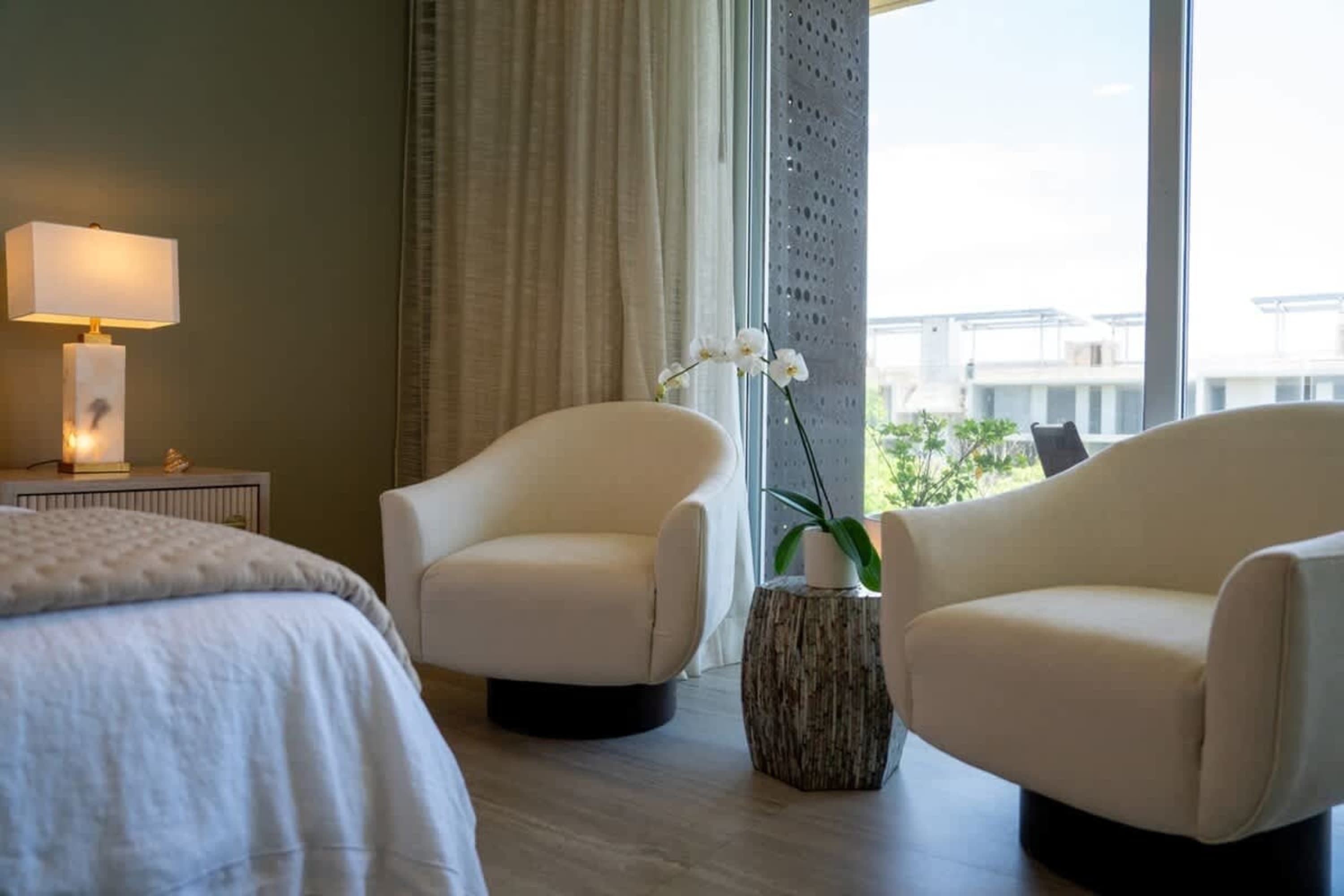A bedroom with a bed, two armchairs, and a lamp next to the bed.