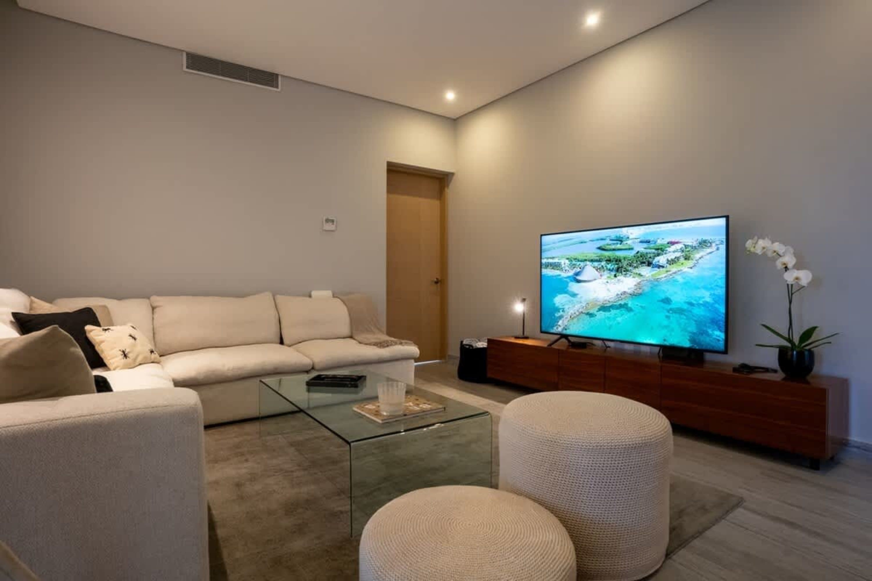 A modern living room with a beige sectional sofa, glass coffee table, and a large TV displaying a tr