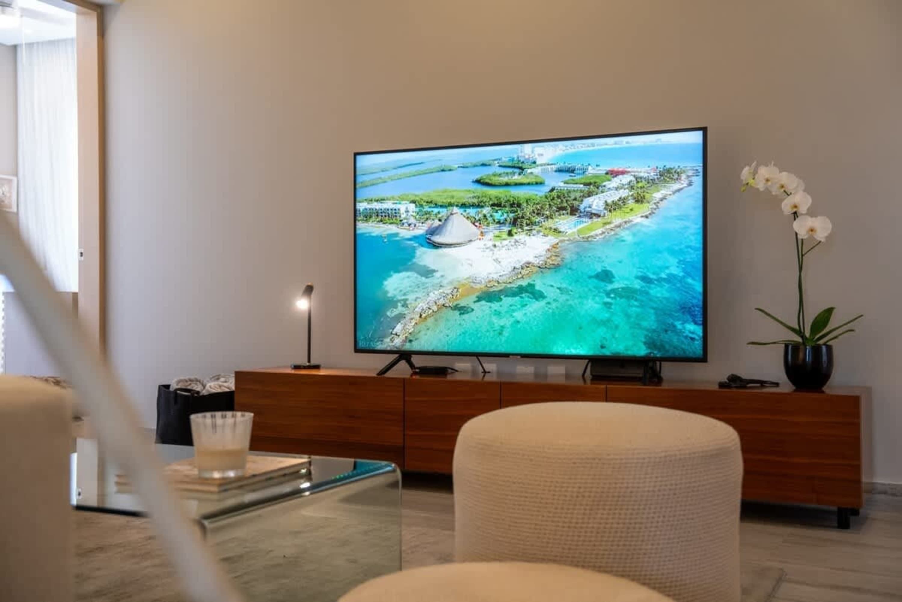 A large TV displays a tropical island resort, next to an orchid.
