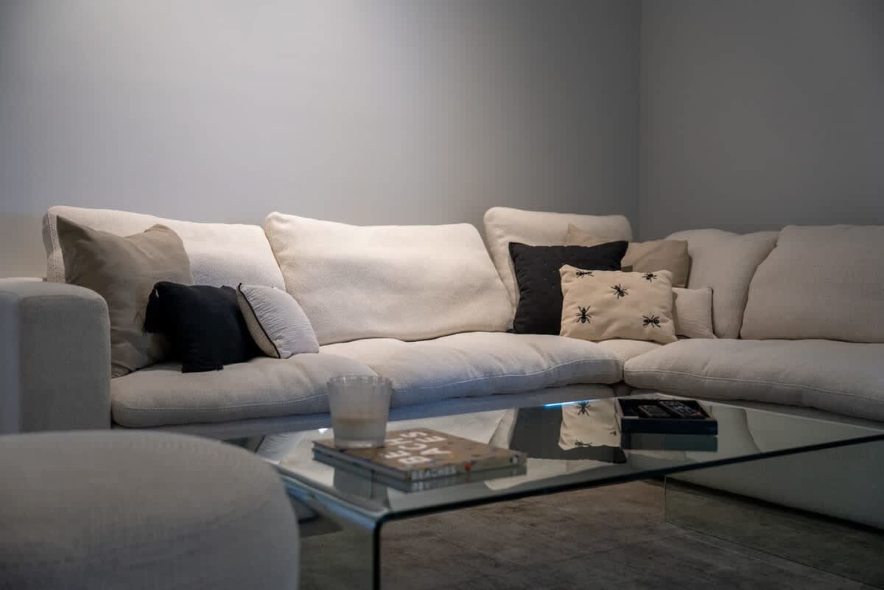 A sectional couch with cream-colored cushions, black and patterned throw pillows, and a glass coffee