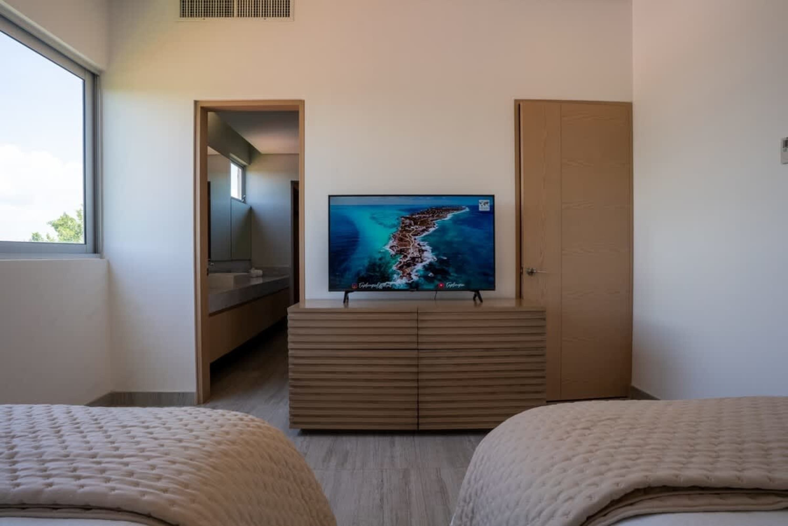 A bedroom with two beds, a TV, and a doorway leading to a bathroom.