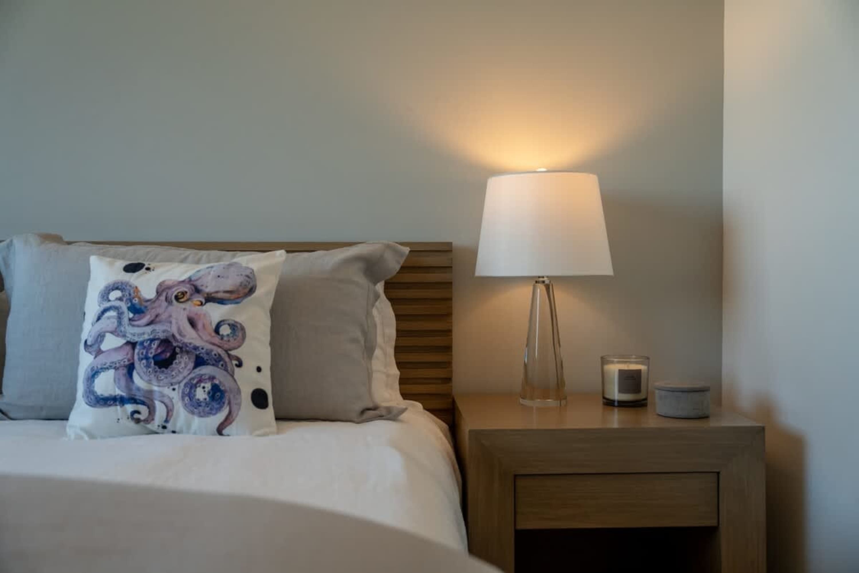 A bedside lamp illuminates a nightstand with a candle and a small decorative jar.