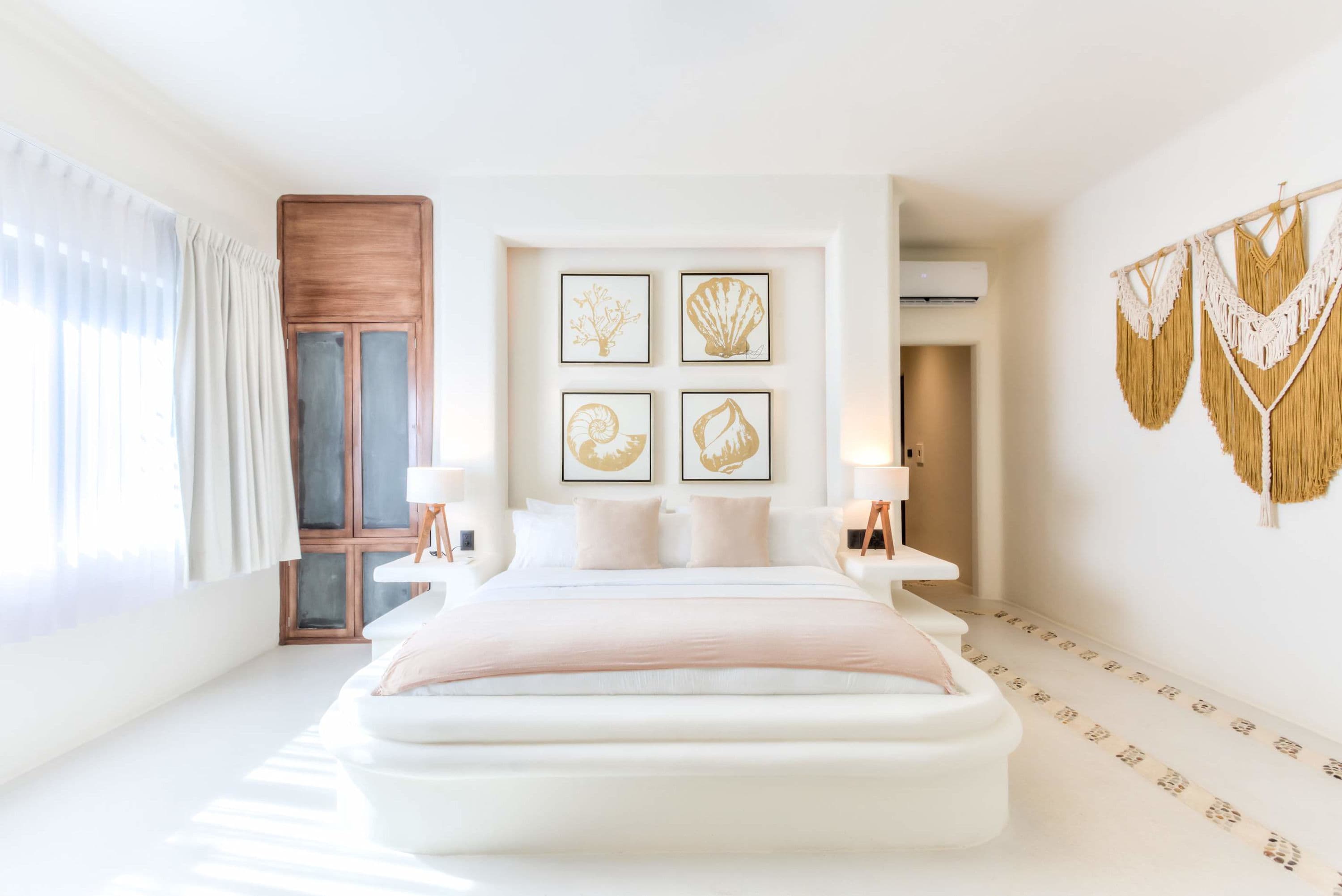 A bright and airy bedroom featuring a large white bed with blush pink accents and nautical-themed wa