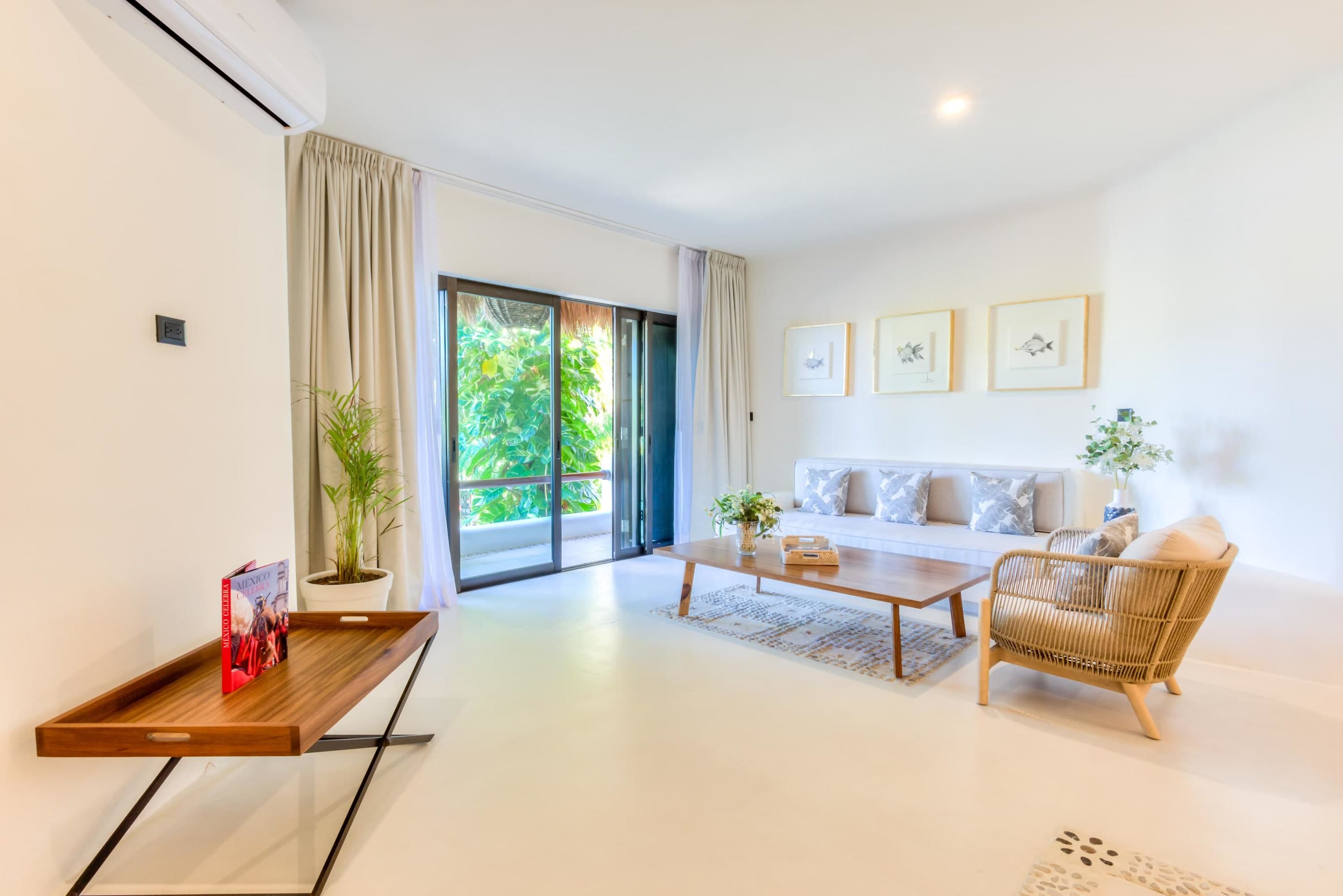 A bright living room features a white sofa, woven armchair, wooden coffee table, and sliding glass d