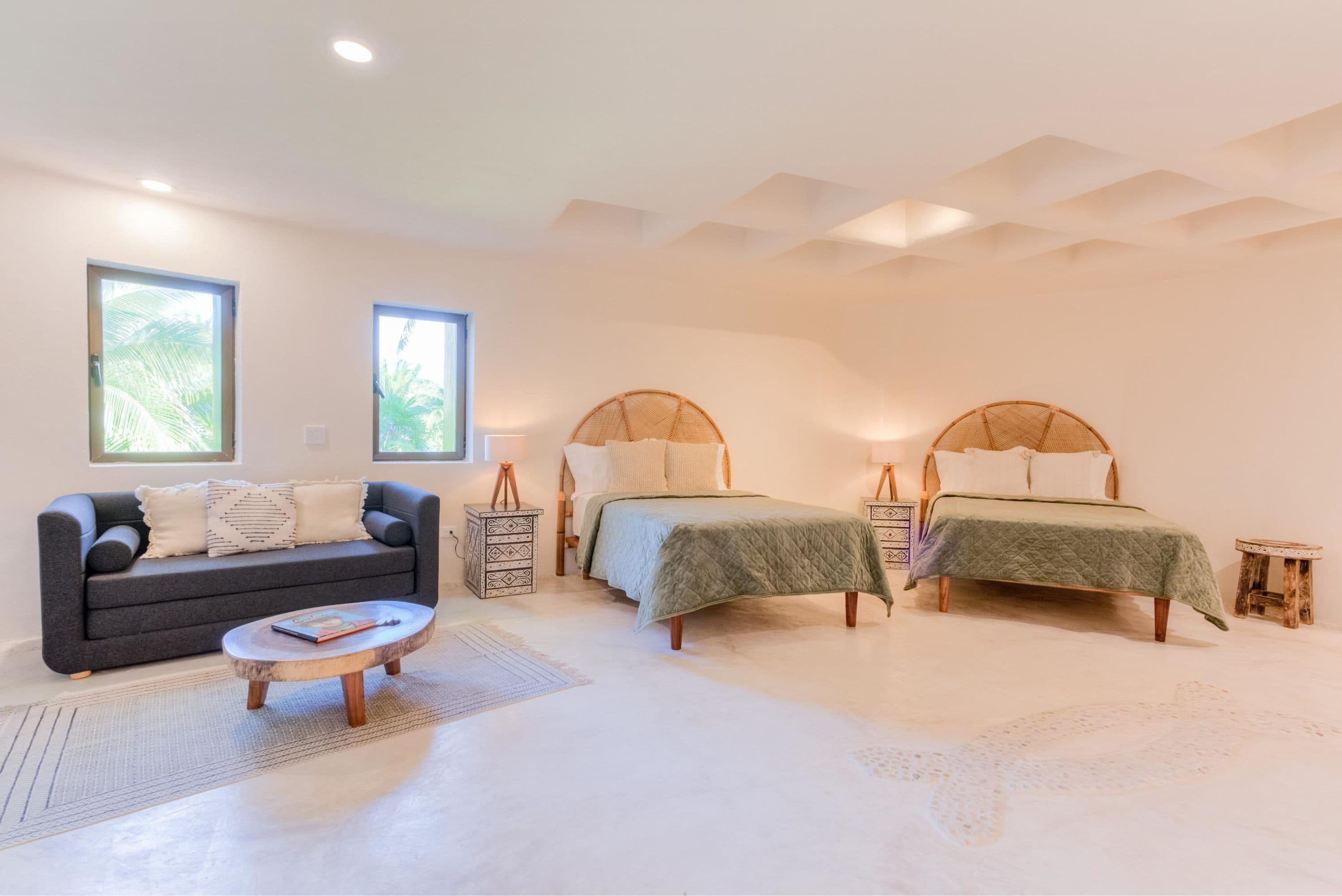 A minimalist bedroom with two beds, a sofa, and large windows.