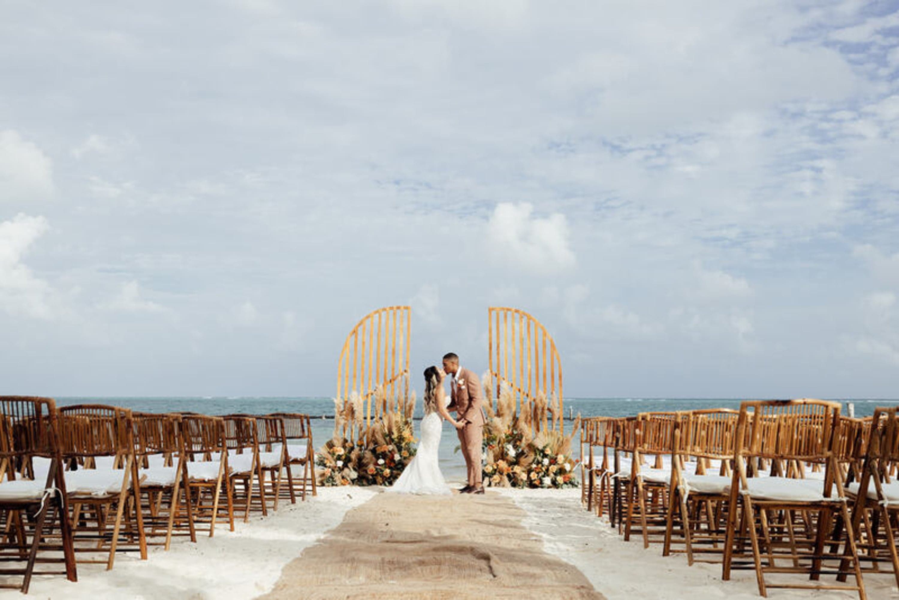 Wedding ceremony on a beach with a bride and groom kissing at the altar.