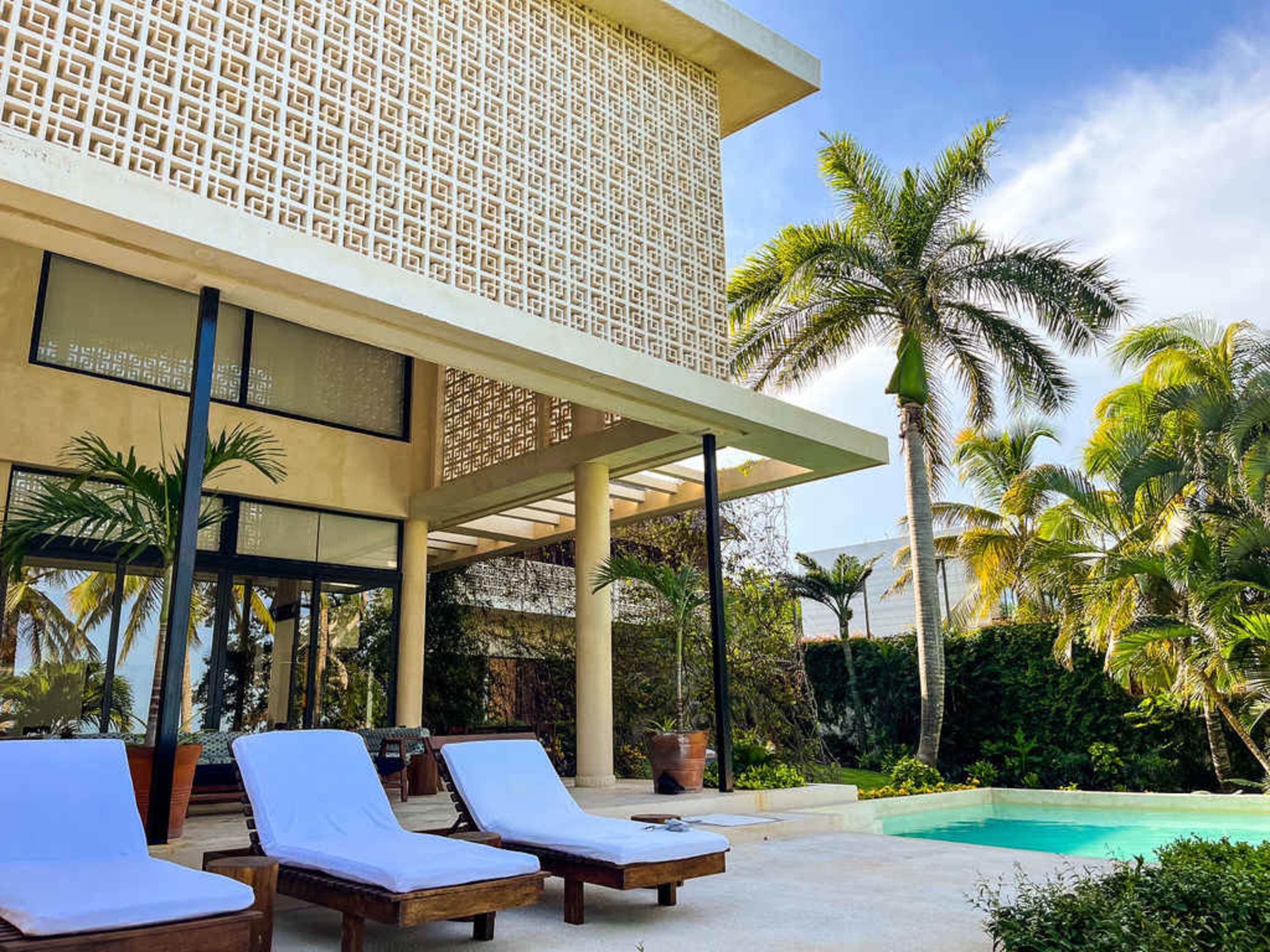 A modern house with a patterned facade and lounge chairs by a swimming pool.