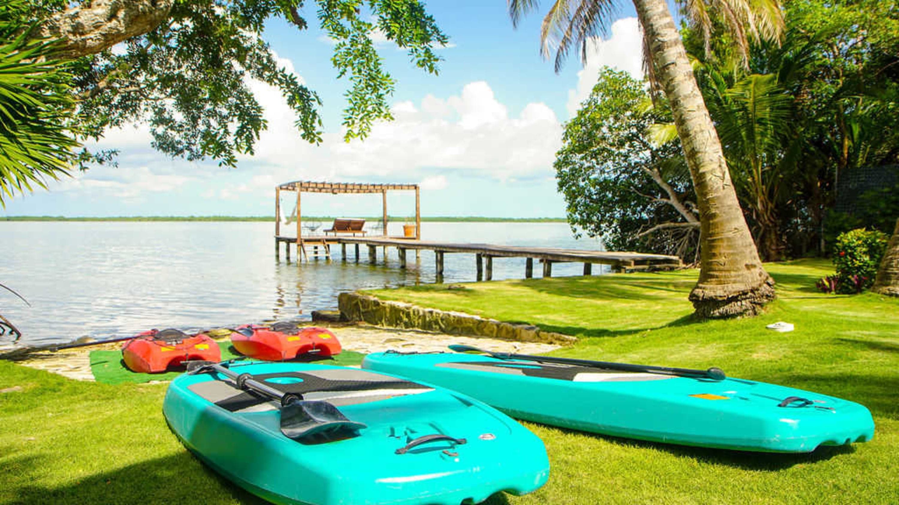 A tranquil tropical scene with paddleboards, kayaks, and a wooden pier on a lake.