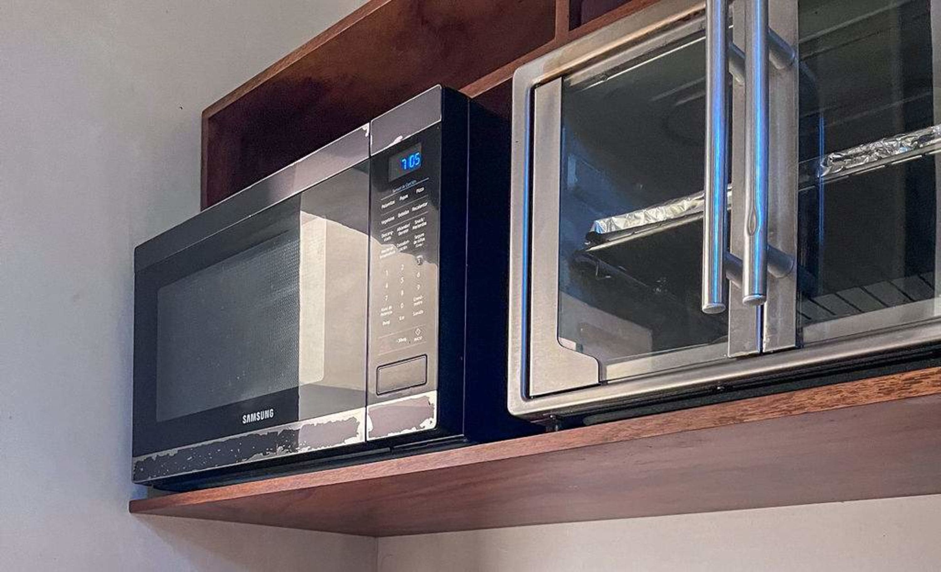 Two kitchen appliances, a microwave and a toaster oven, sit on a wooden shelf.