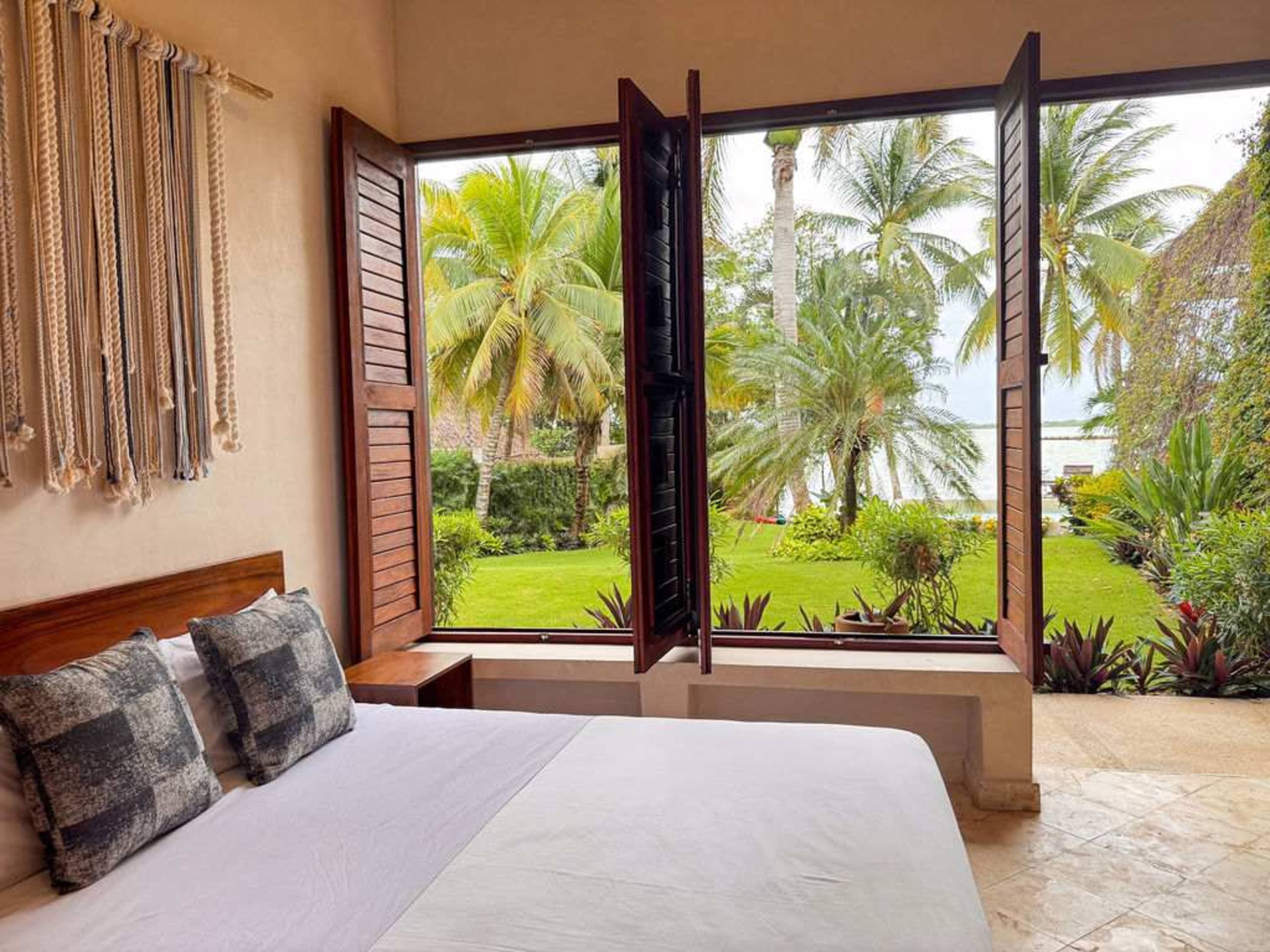 Bedroom with a view of a tropical garden and a body of water.