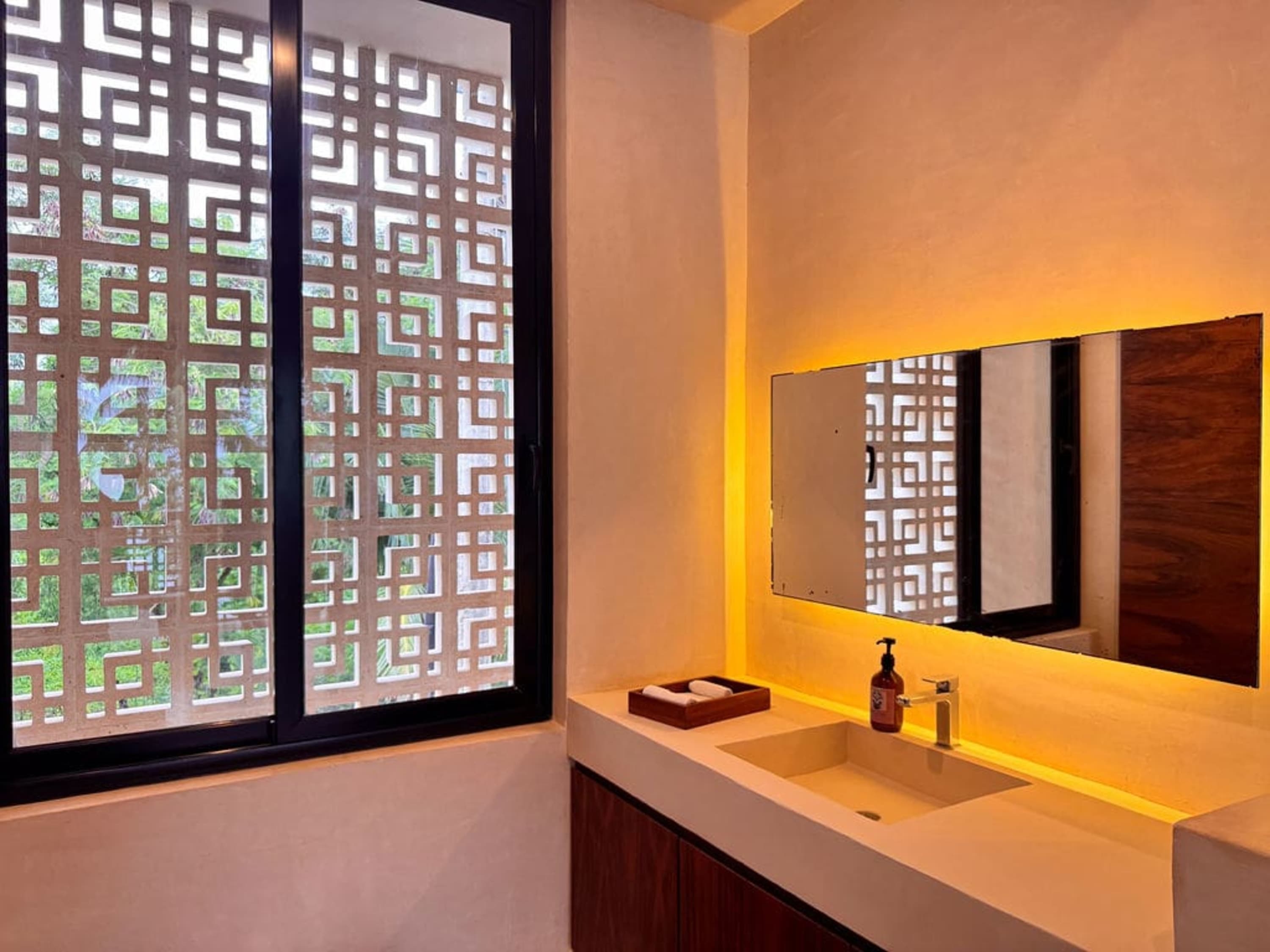 A modern bathroom with a sleek sink, illuminated mirror, and a decorative window.