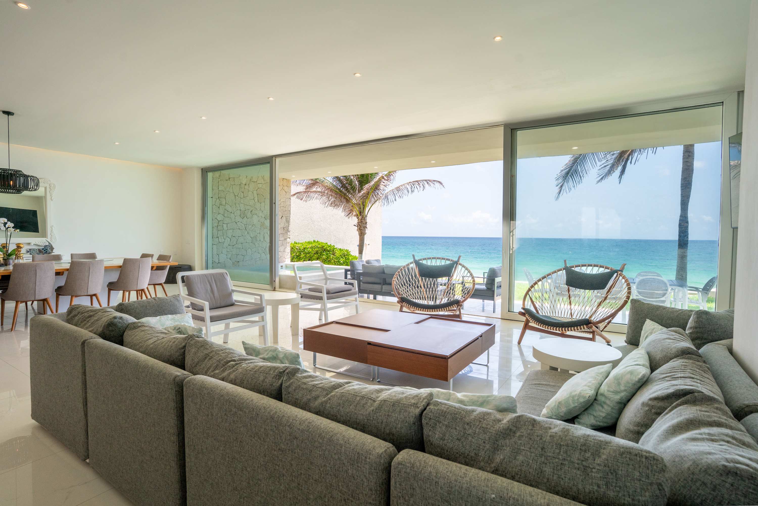 Living room with a sectional sofa facing a sliding glass door open to a beach and ocean view.